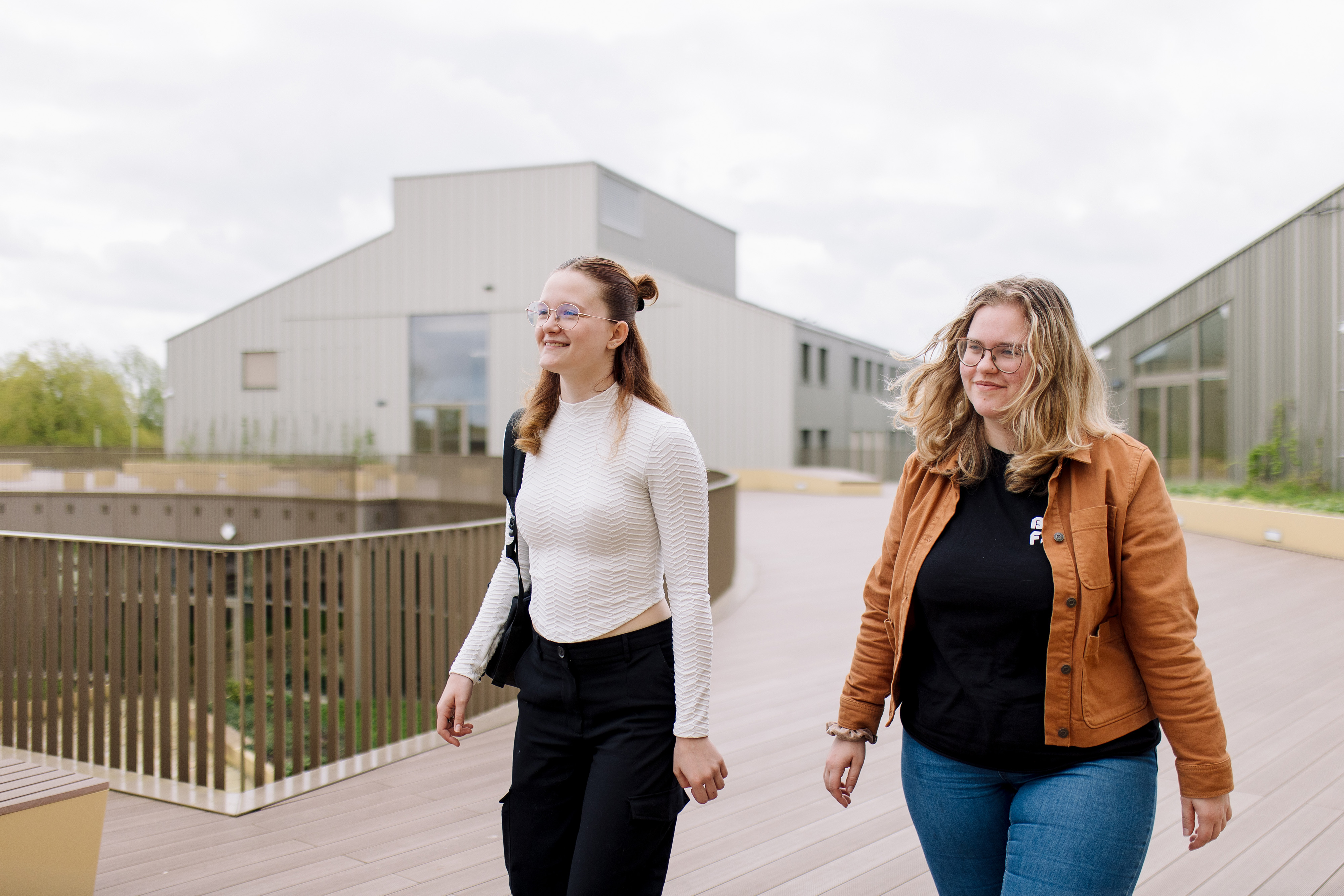 Twee studenten lopen samen op een pad bij het schoolgebouw van Noorderpoort in Noord-Nederland