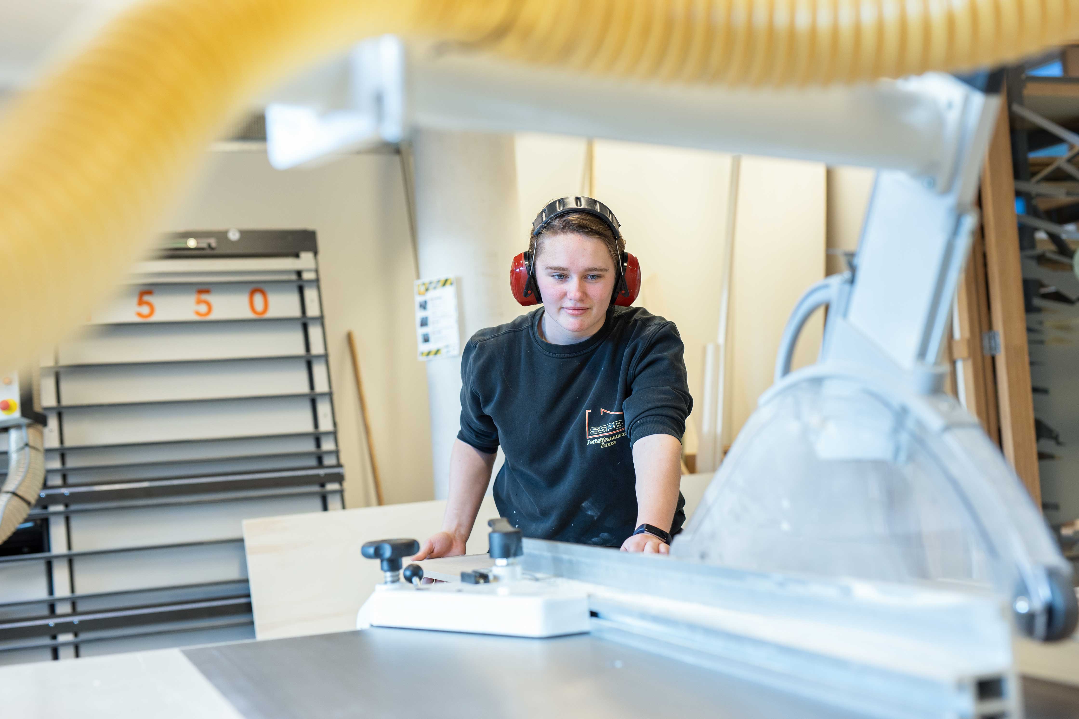 MBO-student werkt geconcentreerd met houtbewerkingsmachine binnen bouwopleidingsomgeving