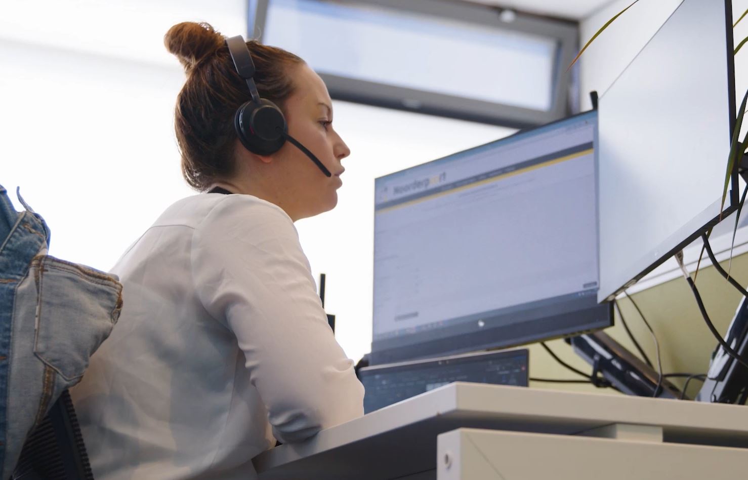 Medewerker in het contactcentrum beantwoordt vragen via een headset aan een werkplek met meerdere schermen