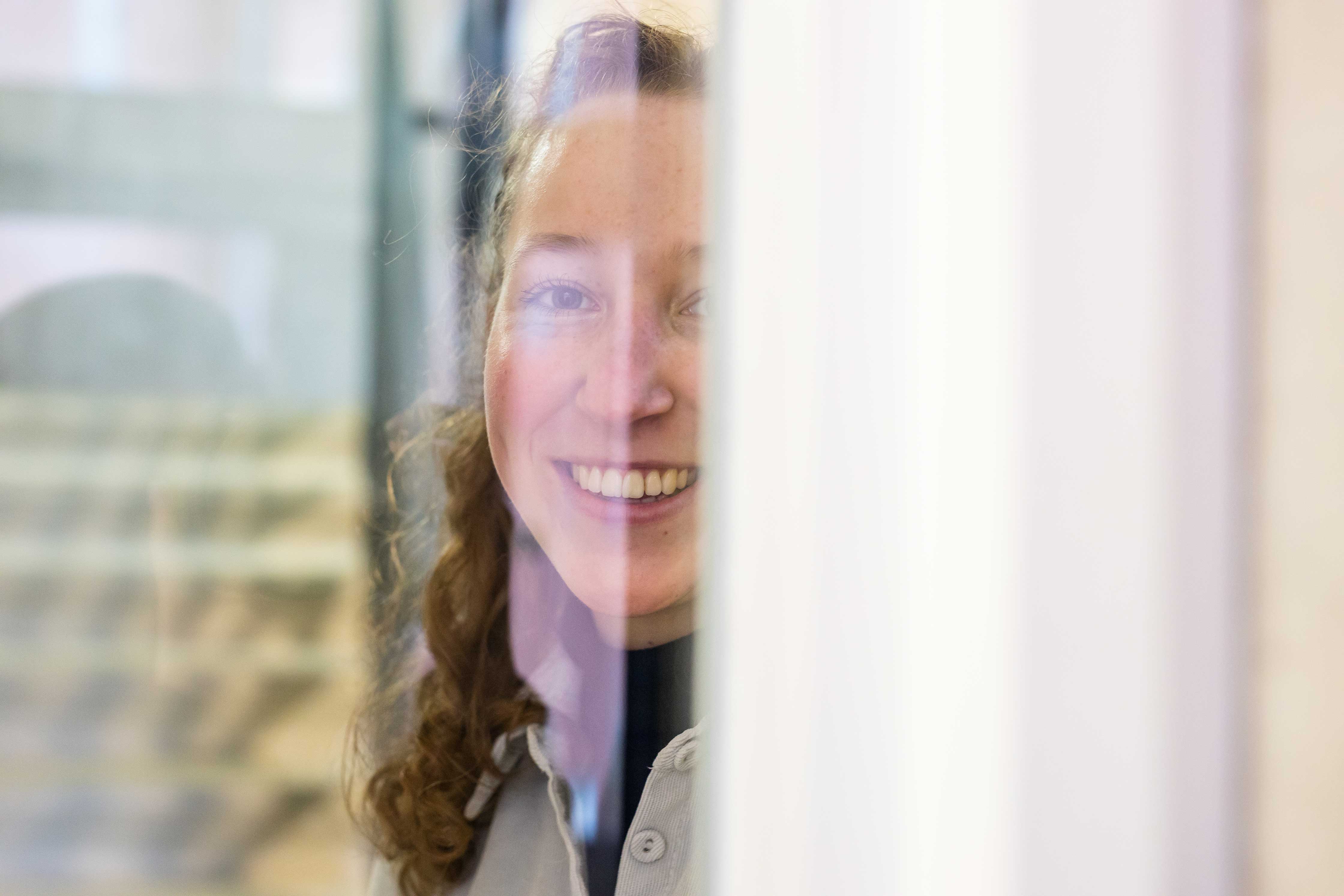 Student kijkt glimlachend door een raam, gericht op persoonlijke groei en ontwikkeling.