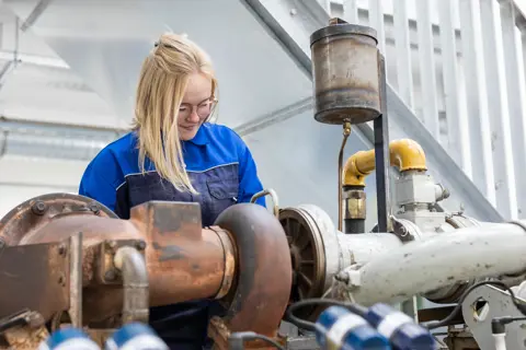 Student in technische werkkleding inspecteert maritieme machineonderdelen tijdens praktijkles