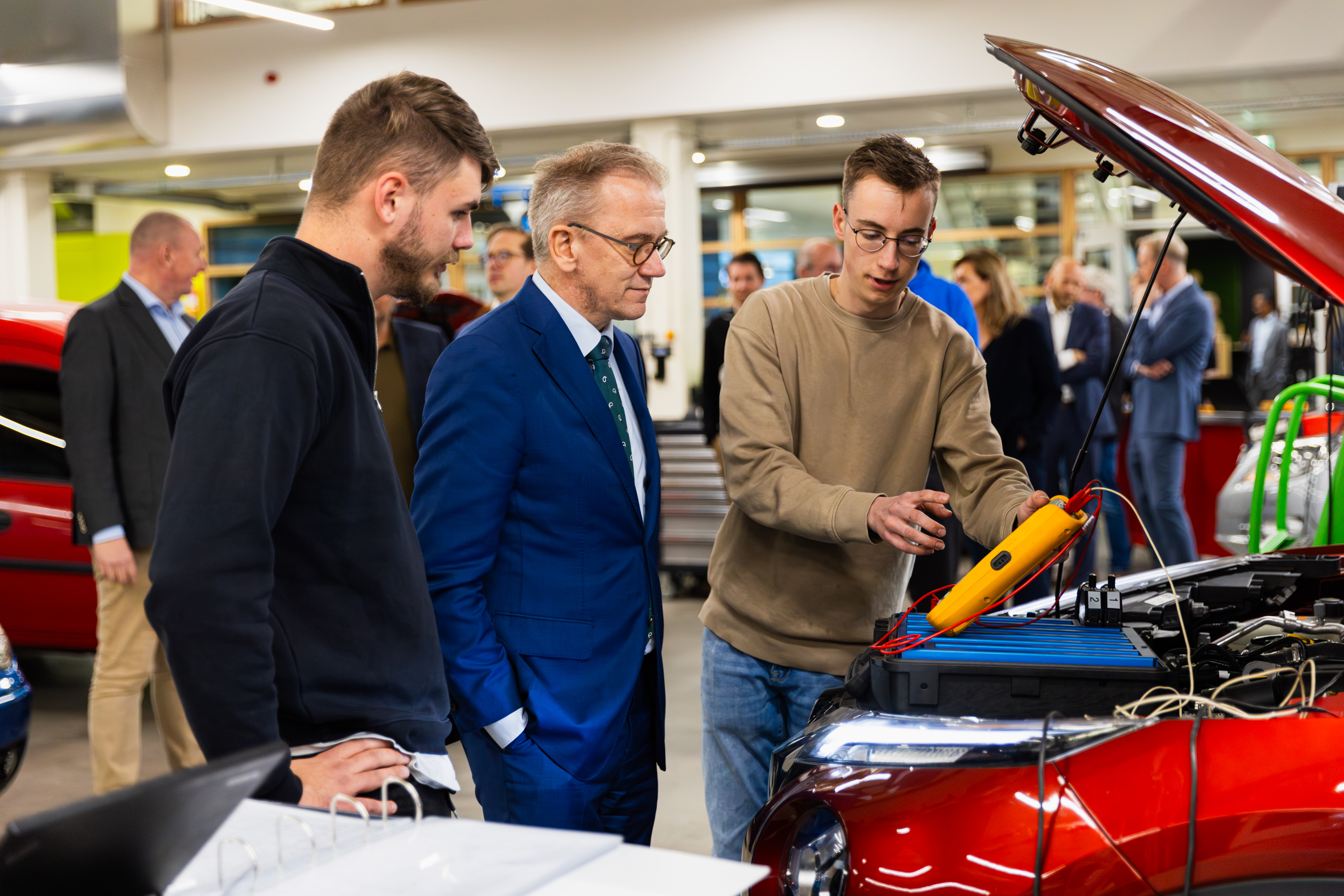 Minister Bruins bekijkt met studenten een elektrische auto in een workshop over mobiliteit van de toekomst