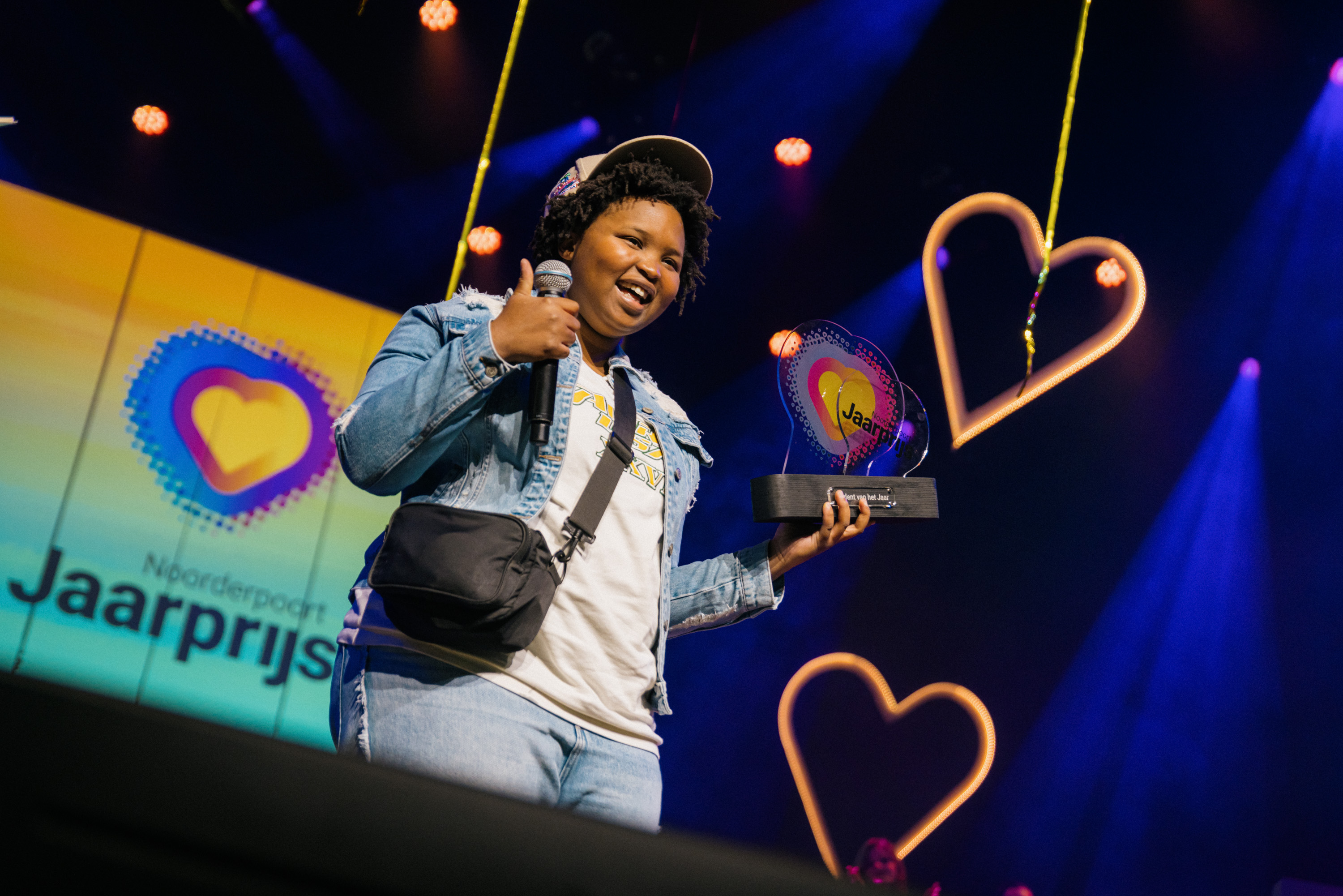 Studente op het podium met een microfoon in de hand en het Noorderpoort Jaarprijs 2024 beeldje
