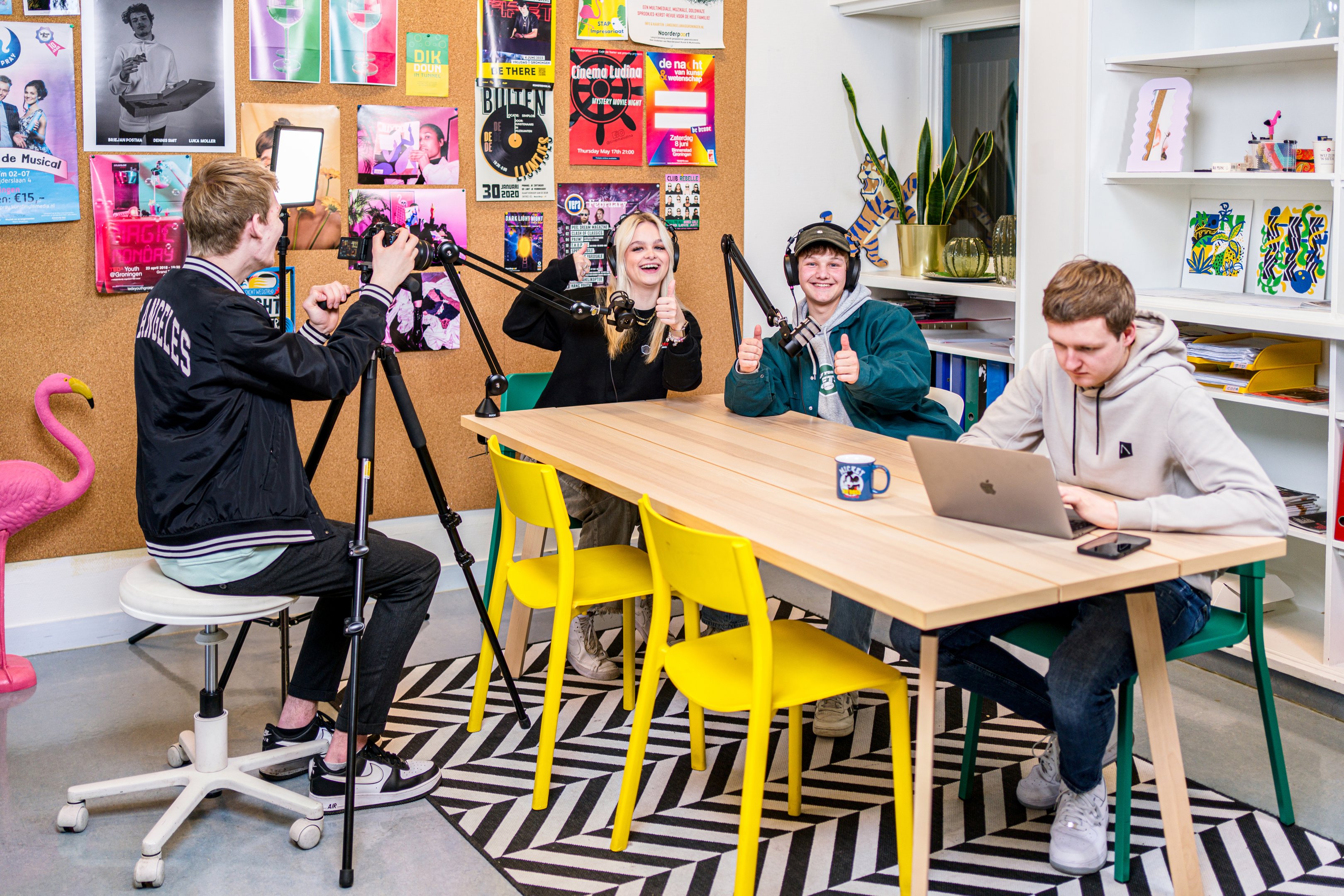 Studenten werken samen aan een creatieve mediaproductie in een kleurrijke ruimte met opnameapparatuur.