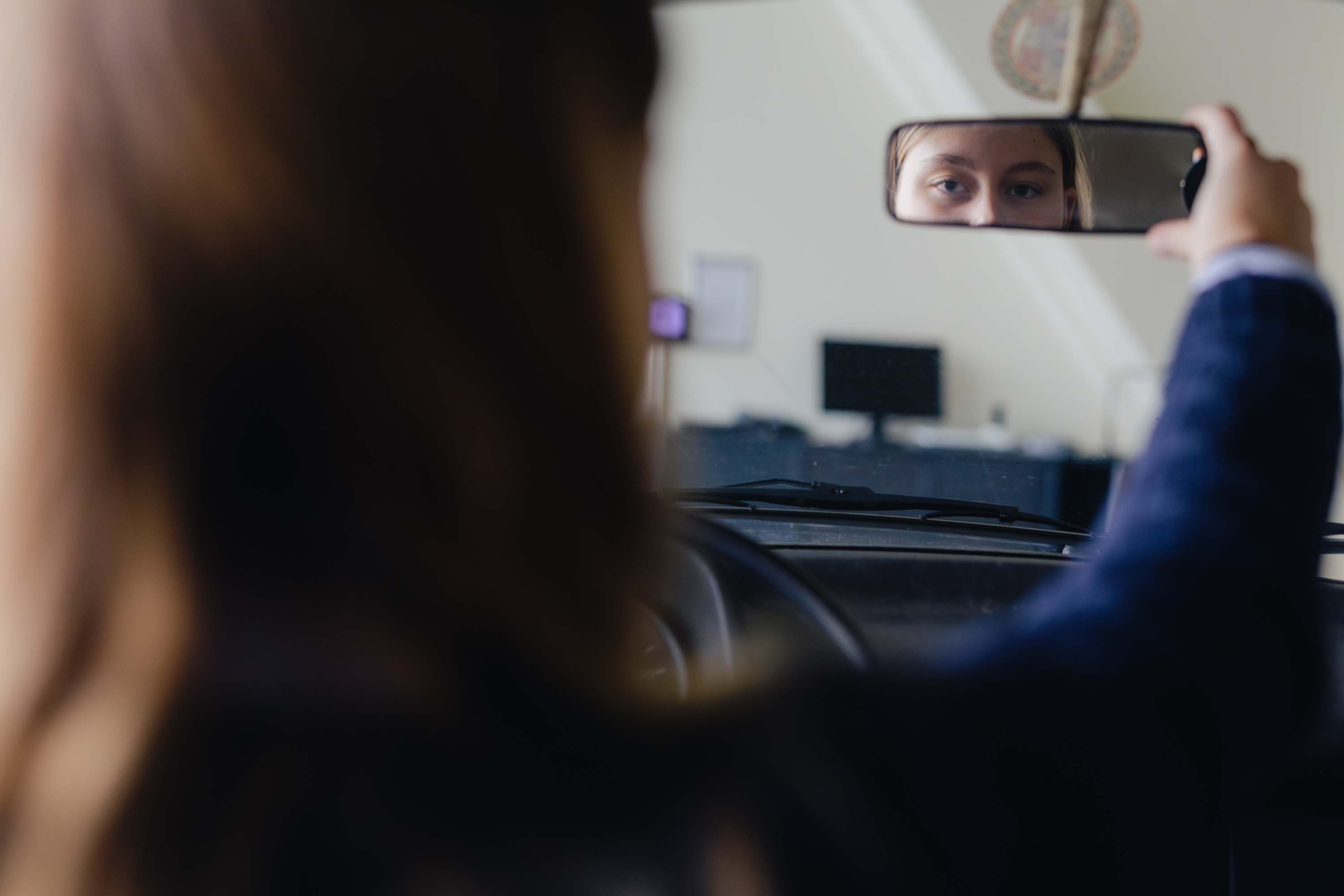 Student controleert zichzelf in de achteruitkijkspiegel tijdens een praktijkles autorijden