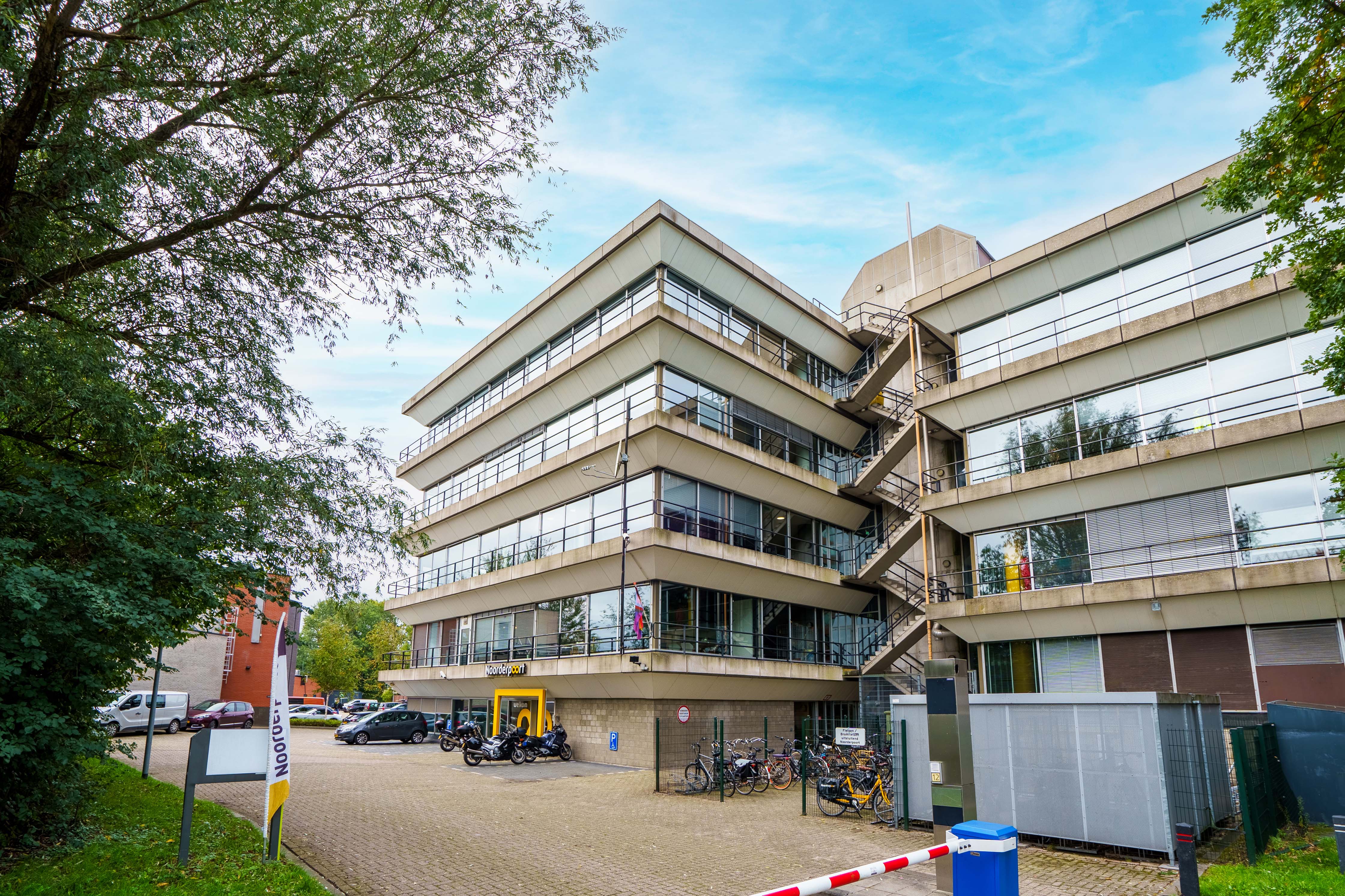 Moderne schoolgebouw Noorderpoort aan Winschoterdiep 50 in Groningen met fietsenrekken en parkeerplaats.