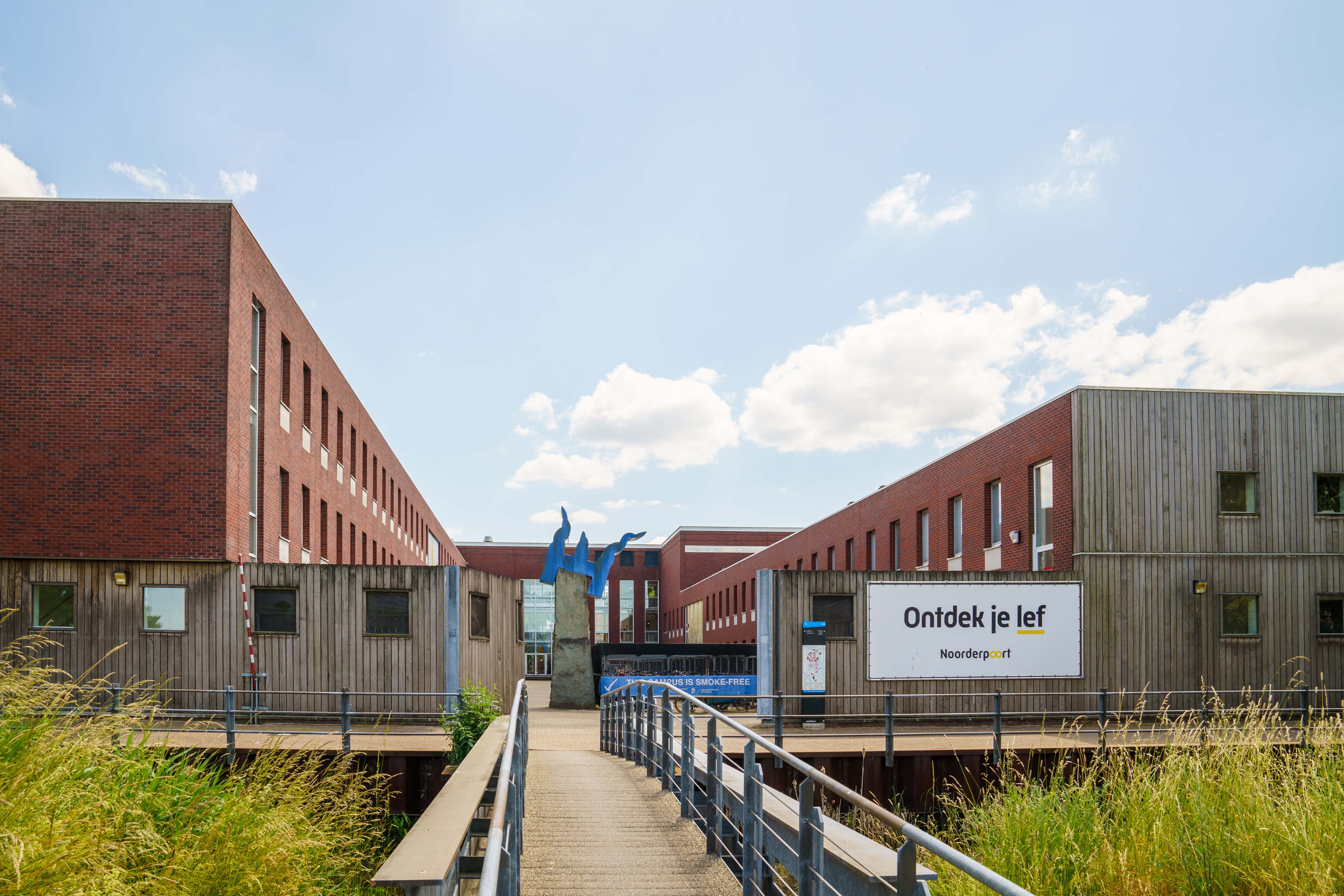 Toegang tot het onderwijsgebouw aan Zernikeplein 11 met een brug en het bord 'Ontdek je lef' van Noorderpoort.