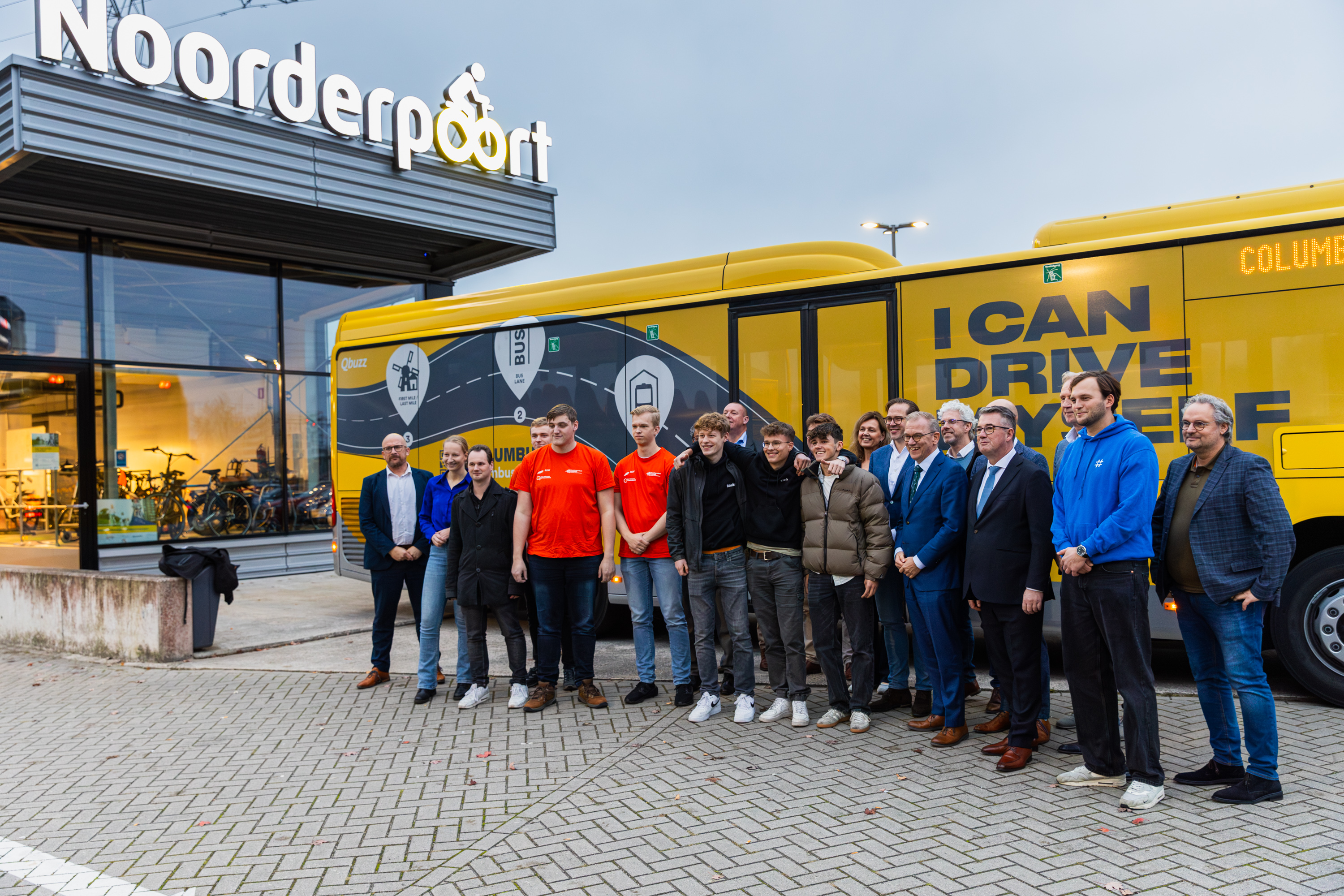 Groep studenten en professionals staan samen voor een gele bus met 'I CAN DRIVE' bij Noorderpoort onderwijsgebouw