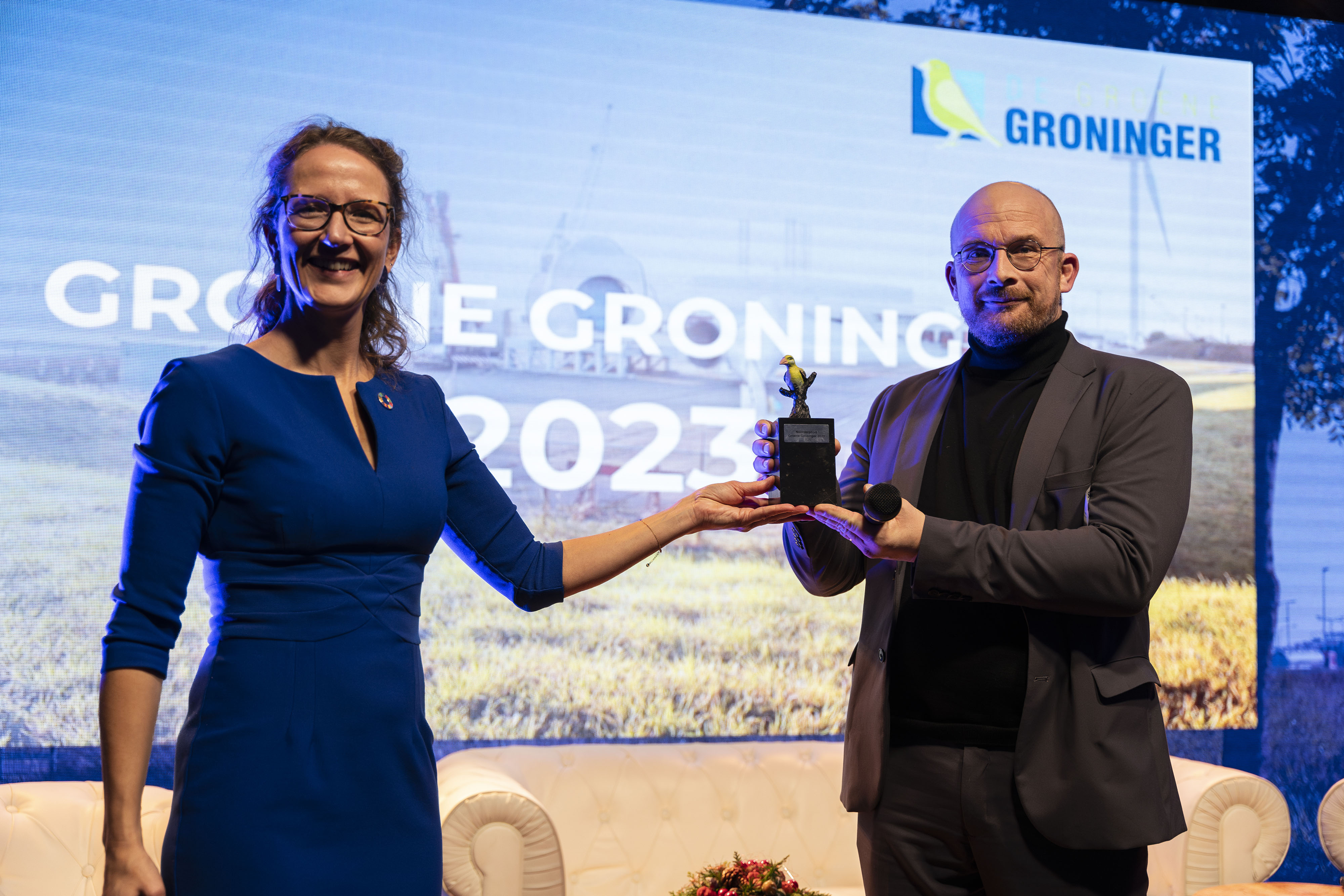 Twee personen overhandigen een prijs op een podium met achtergrondtekst Groene Groninger 2023