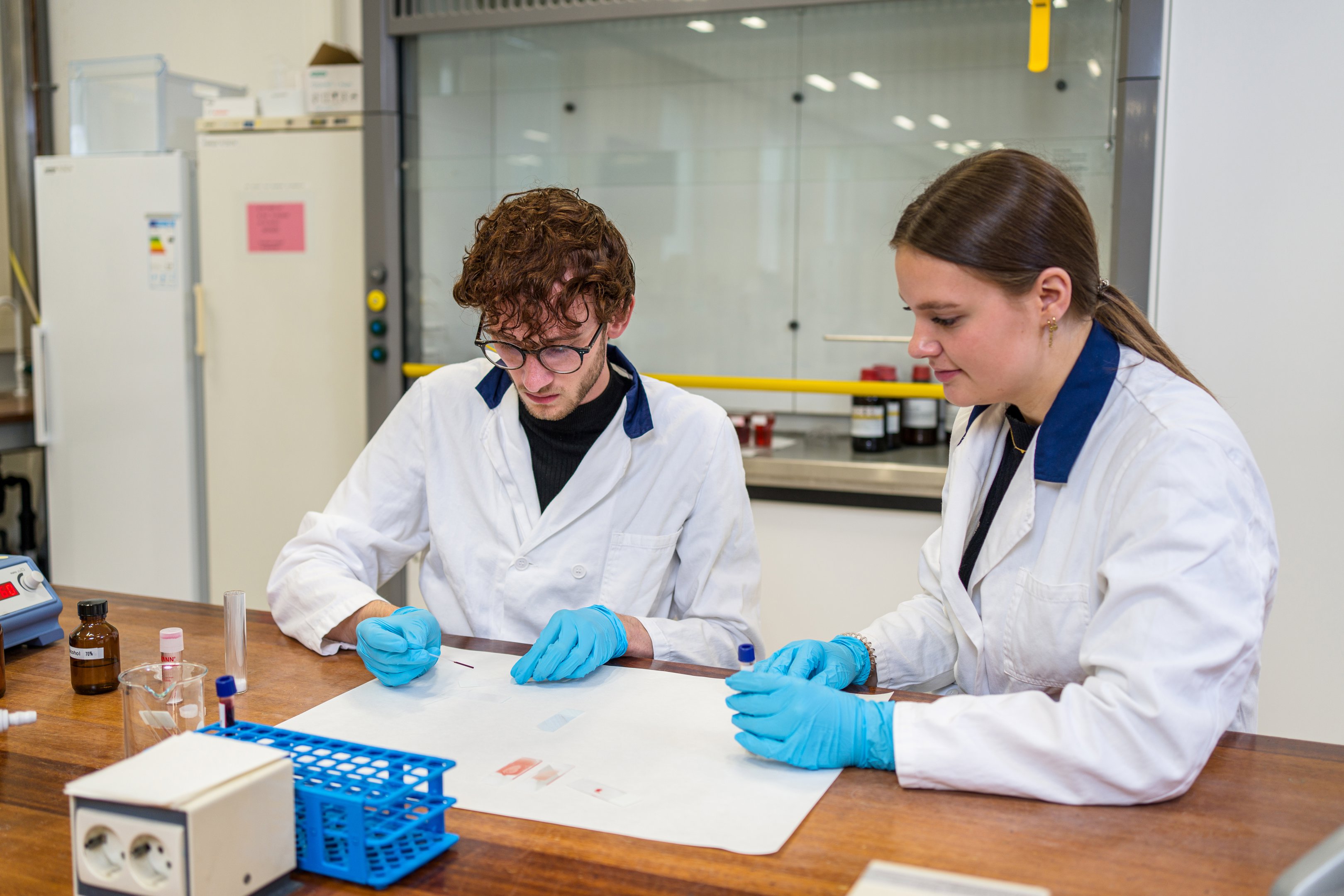 Studenten in laboratoriummantels voeren een wetenschappelijk experiment uit met testmaterialen op een werkbank