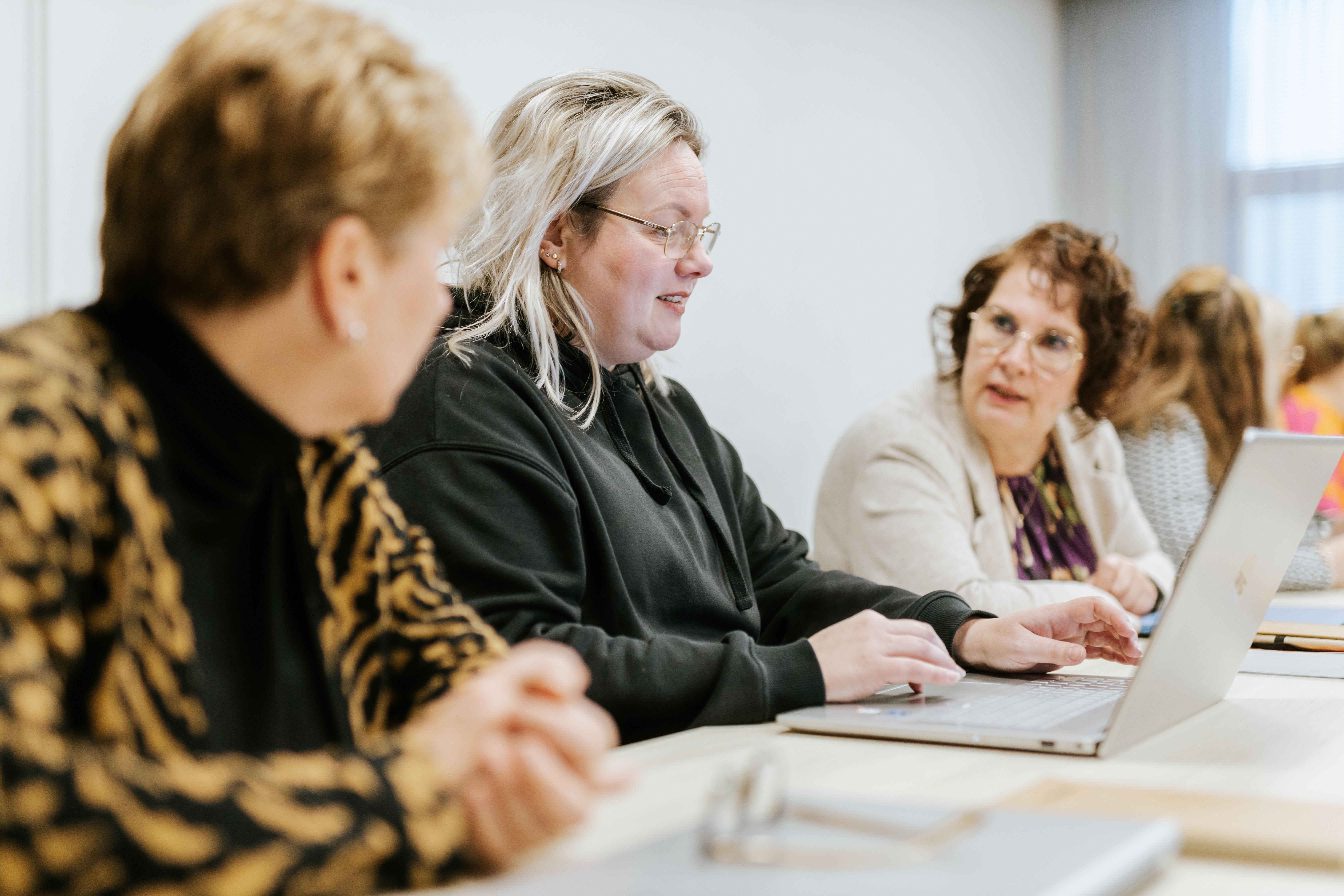 Studenten in gesprek tijdens een praktijkgerichte les over geriatrische zorg met laptops en studiematerialen.