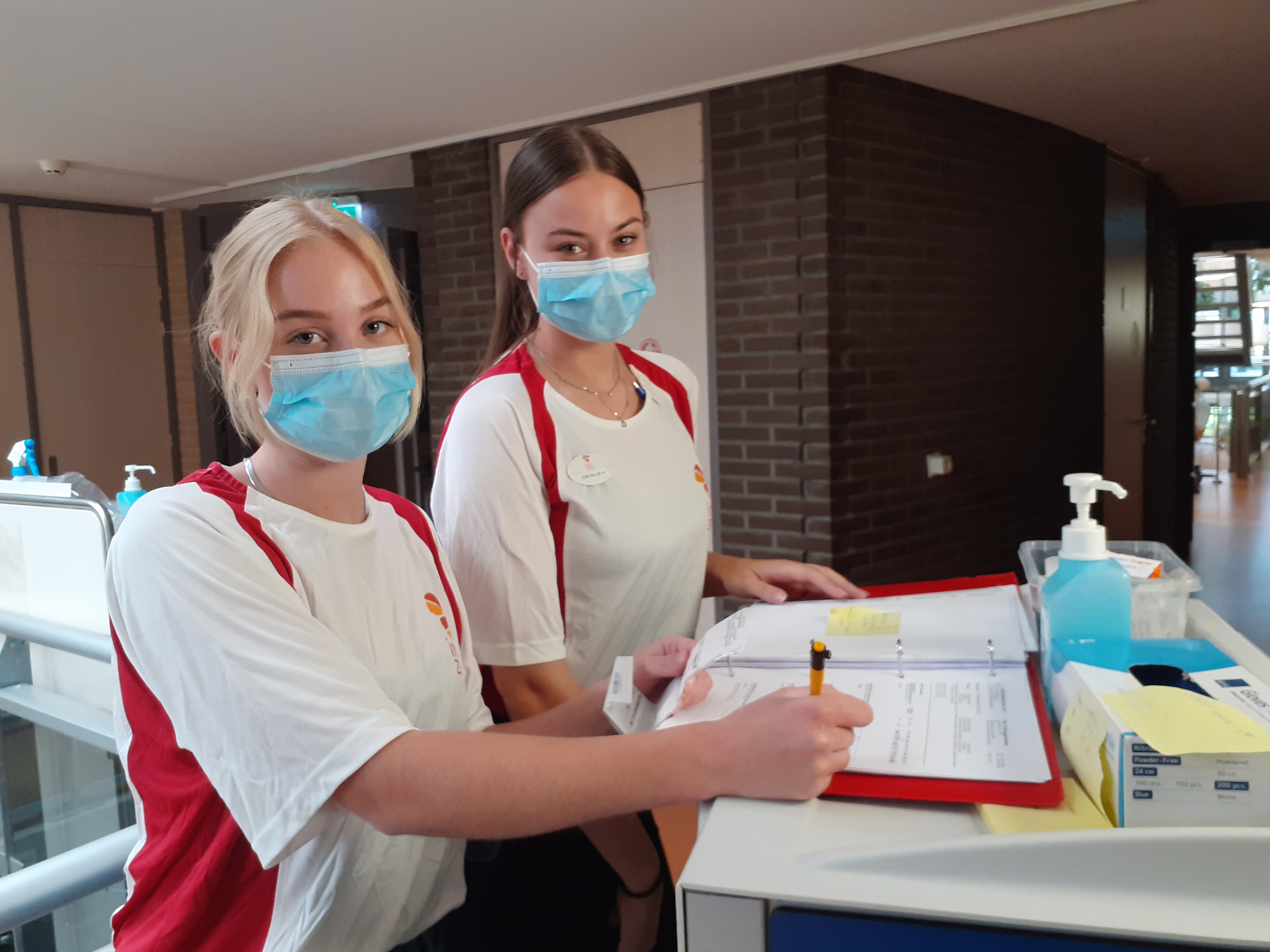 Twee studenten van Noorderpoort met mondkapjes bekijken documenten bij balie in schoolgebouw De Driemaster