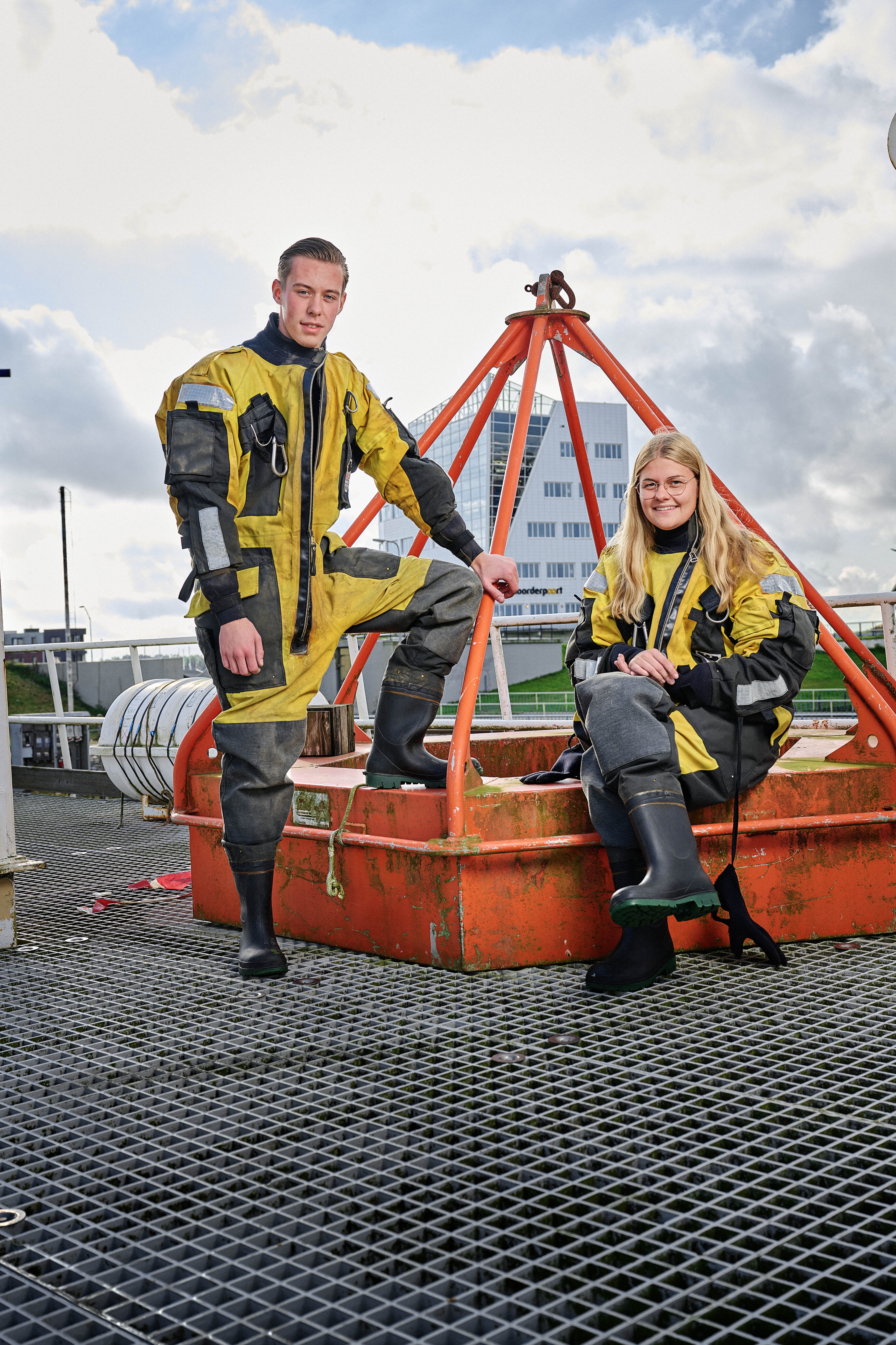 Twee studenten in beschermende kleding bereiden zich voor op een praktijkopdracht in een maritieme leeromgeving.