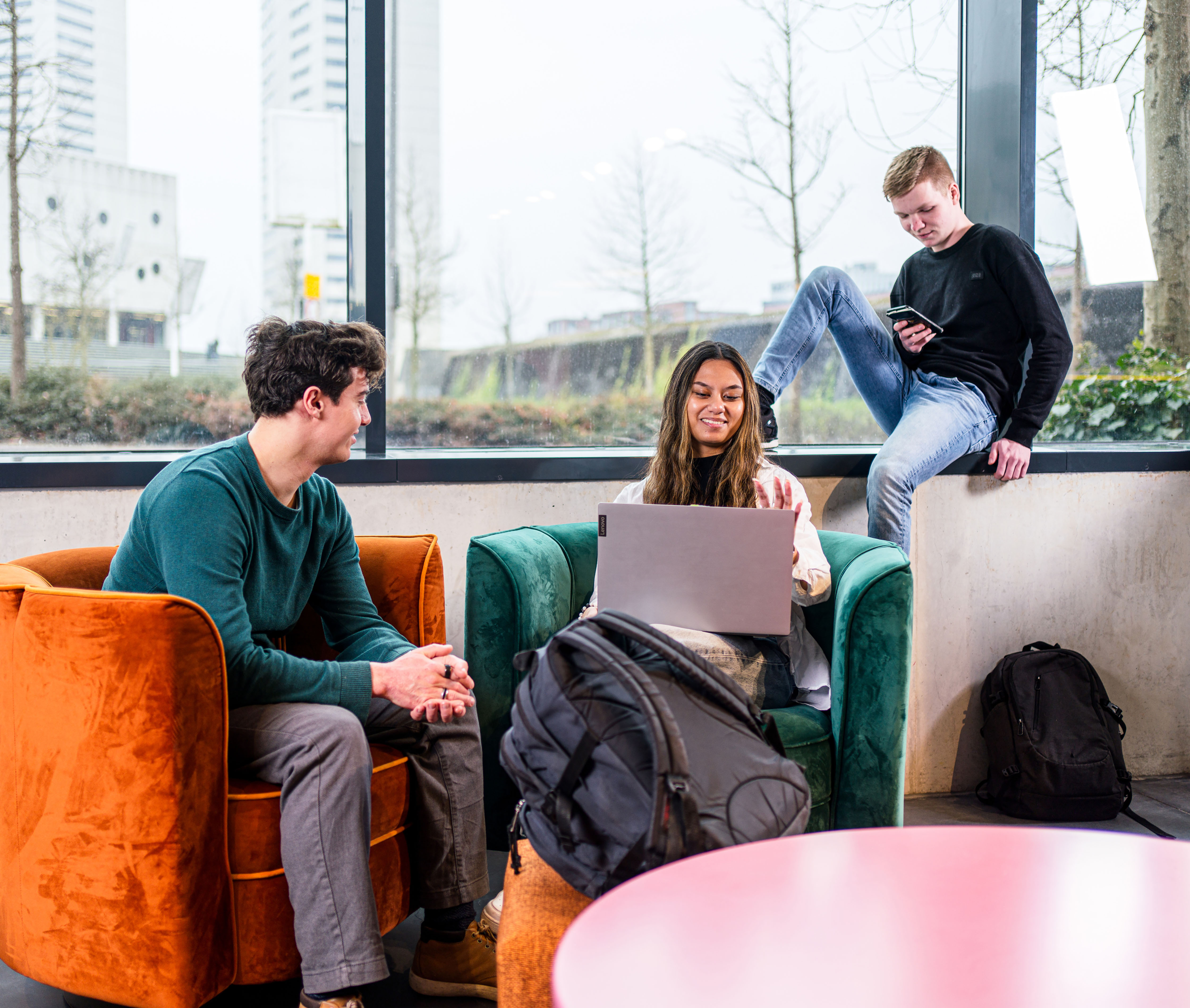 Studenten in ontspanningsruimte bekijken samen informatie op laptop en telefoon