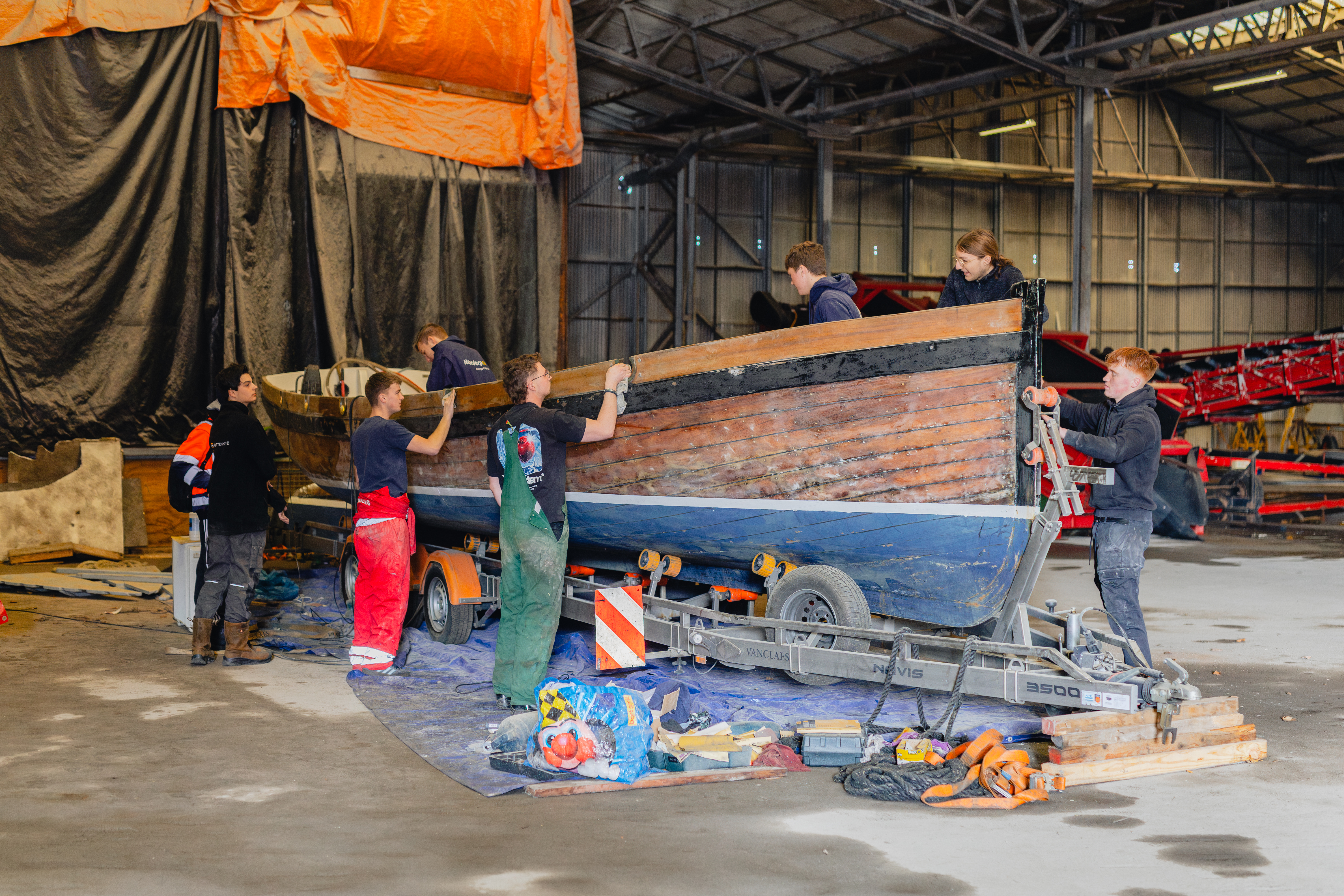 Maritiem studenten dragen gezamenlijk een houten boot in een werkplaats voor restauratie en onderhoud