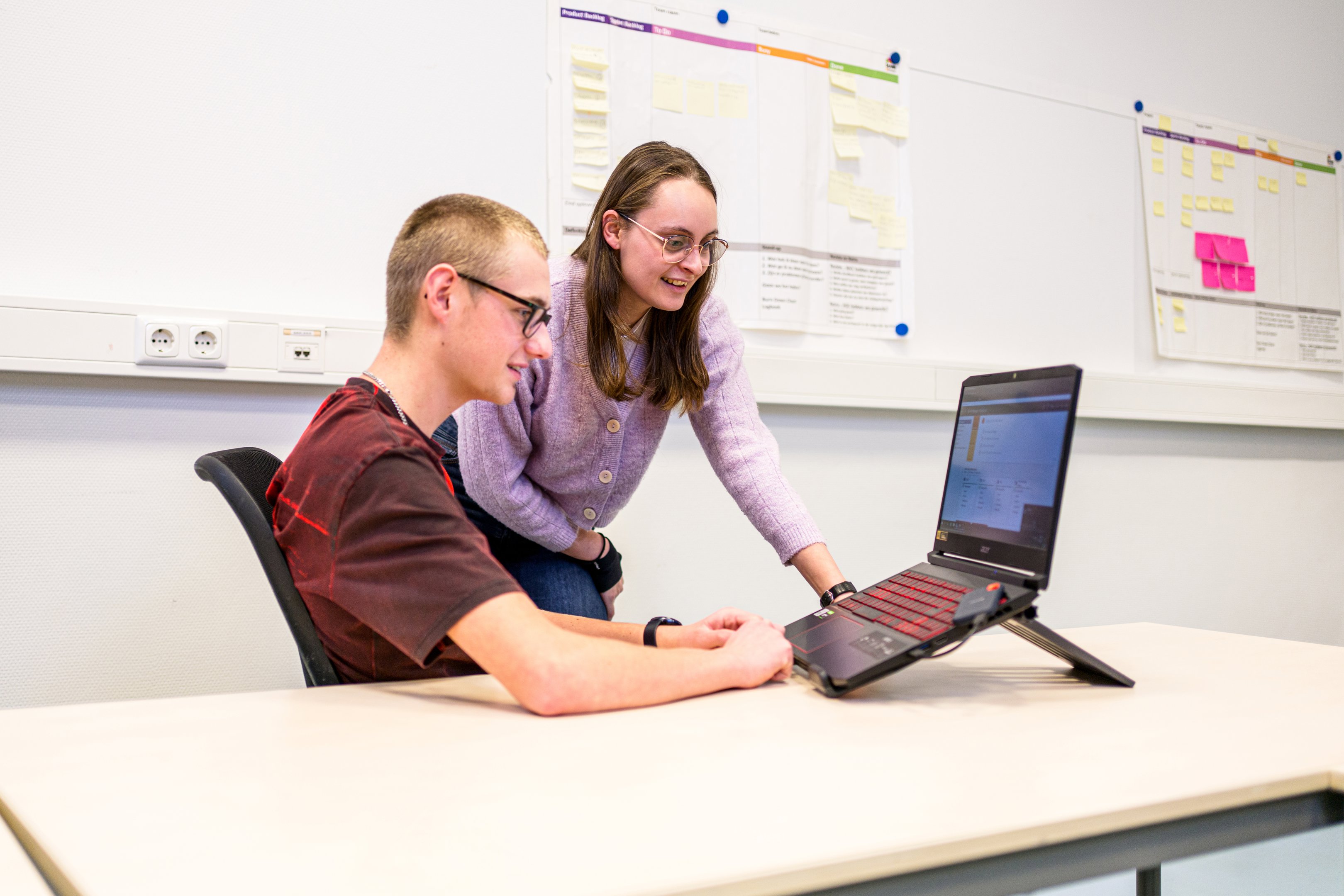 Medewerker en docent bespreken een project op laptop tijdens ICT-opleiding bij Noorderpoort