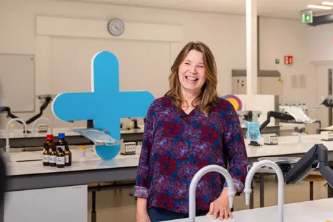 Docent in laboratoriumomgeving lacht trots, benadrukt betrokkenheid bij praktijkgericht technisch onderwijs