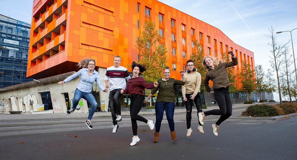 Groep enthousiaste studenten springt voor een modern schoolgebouw in Groningen, startpunt gezamenlijke onderwijsprogramma