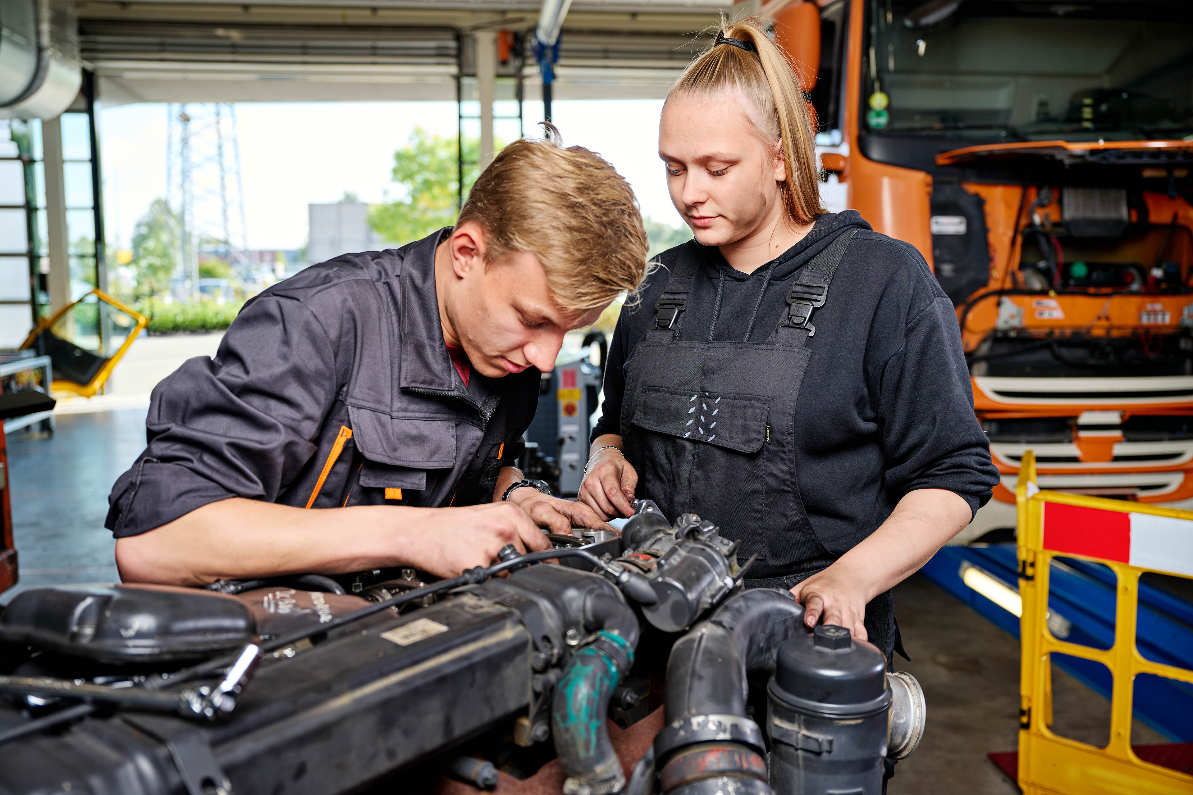 Twee studenten werken samen aan motoronderhoud in een technische leeromgeving.