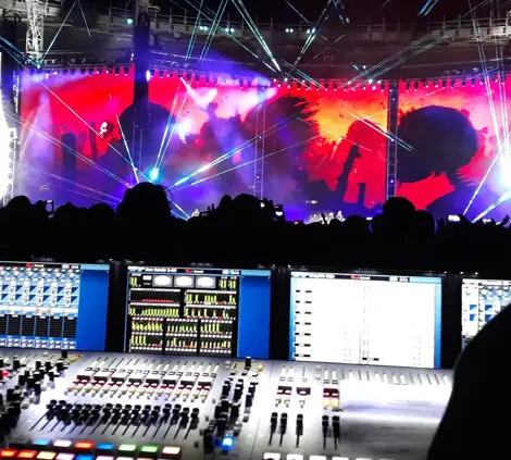 Technicus bedient een geluids- en lichtpaneel tijdens een live evenement met kleurrijke projecties op de achtergrond