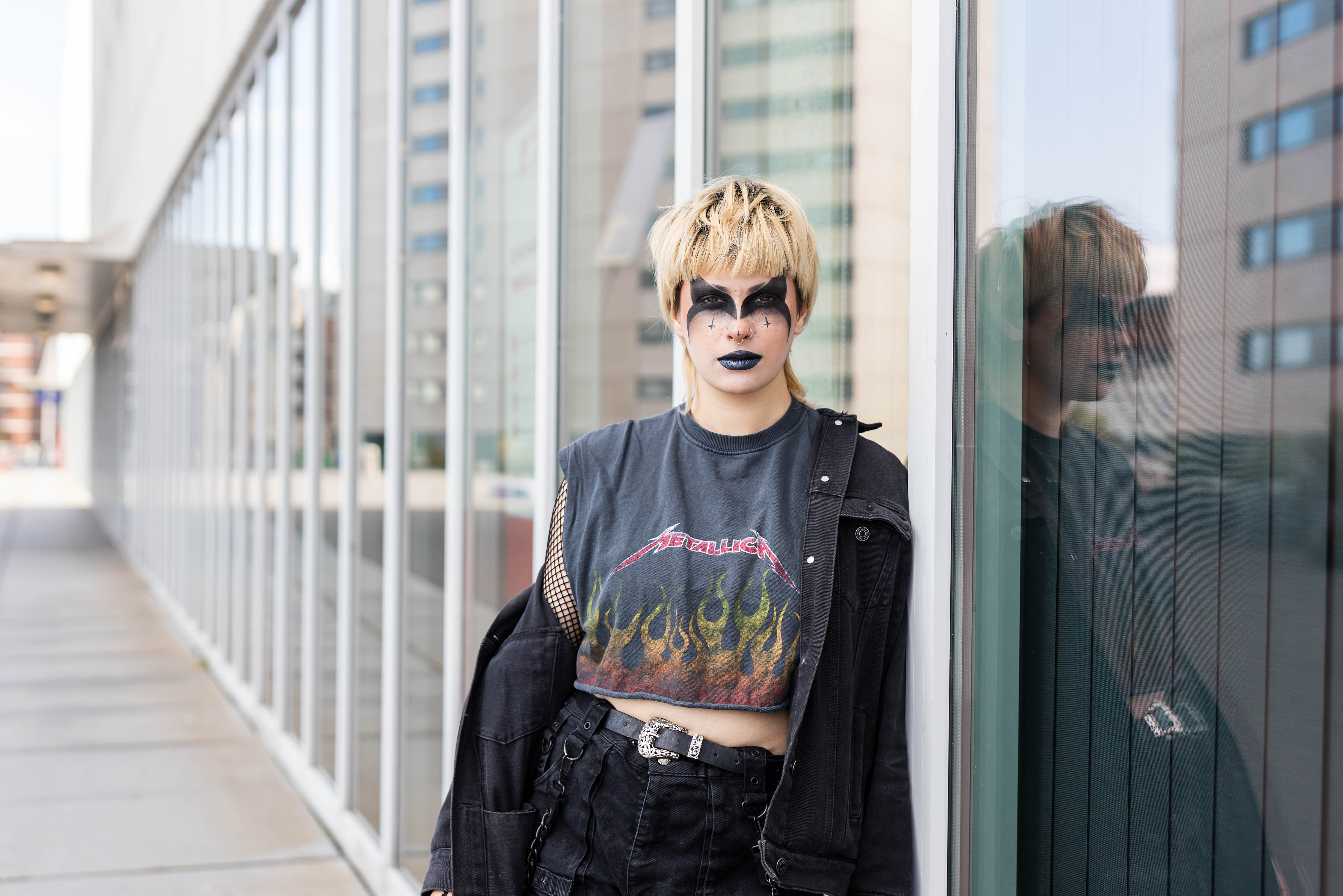 Student met creatieve make-up poseert buiten tegen een glazen gevel van een modern gebouw