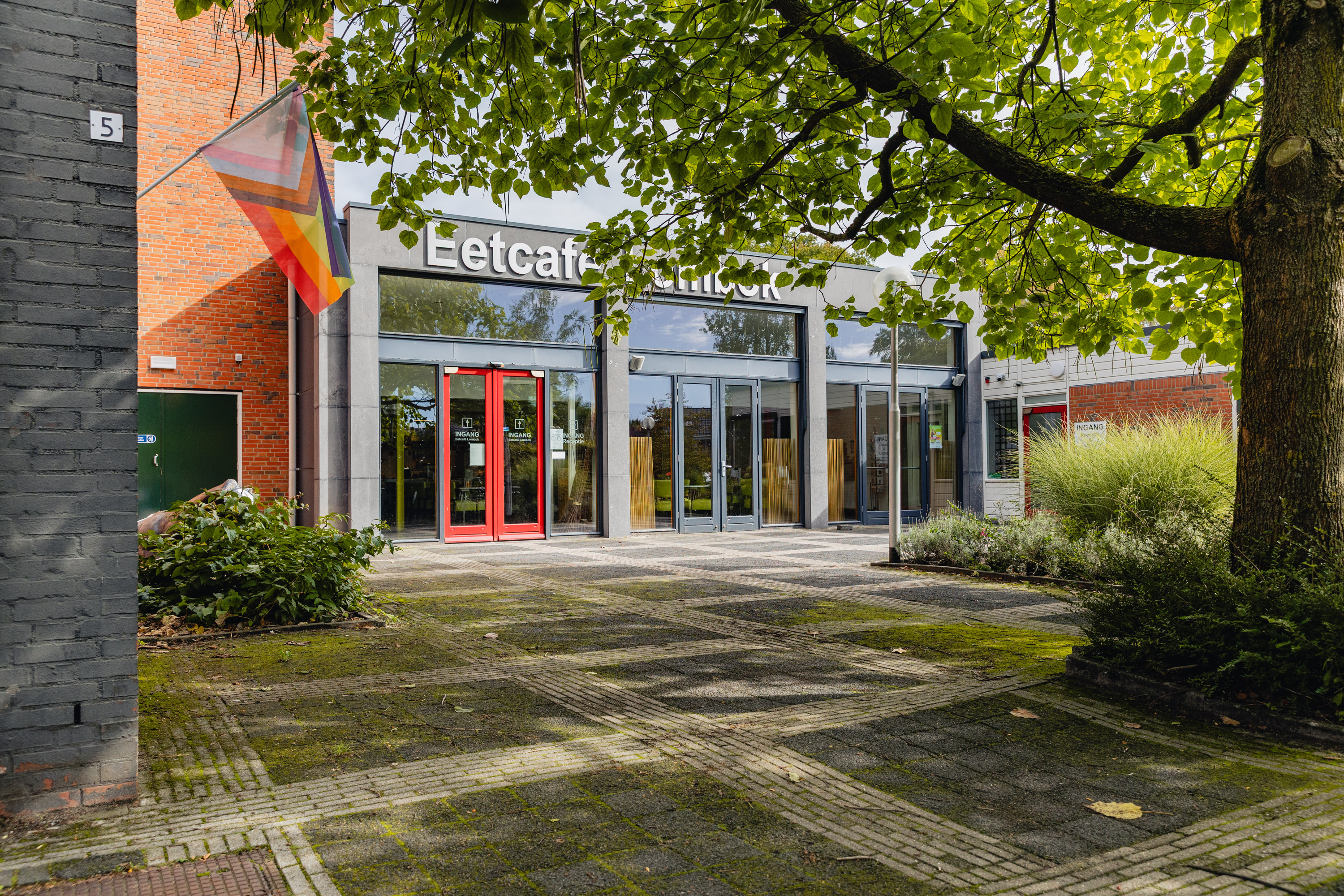 Hoofdingang van Noorderpoort locatie Hendrik van Boeijenlaan 5 in Assen met bord eetcafé en groen rondom