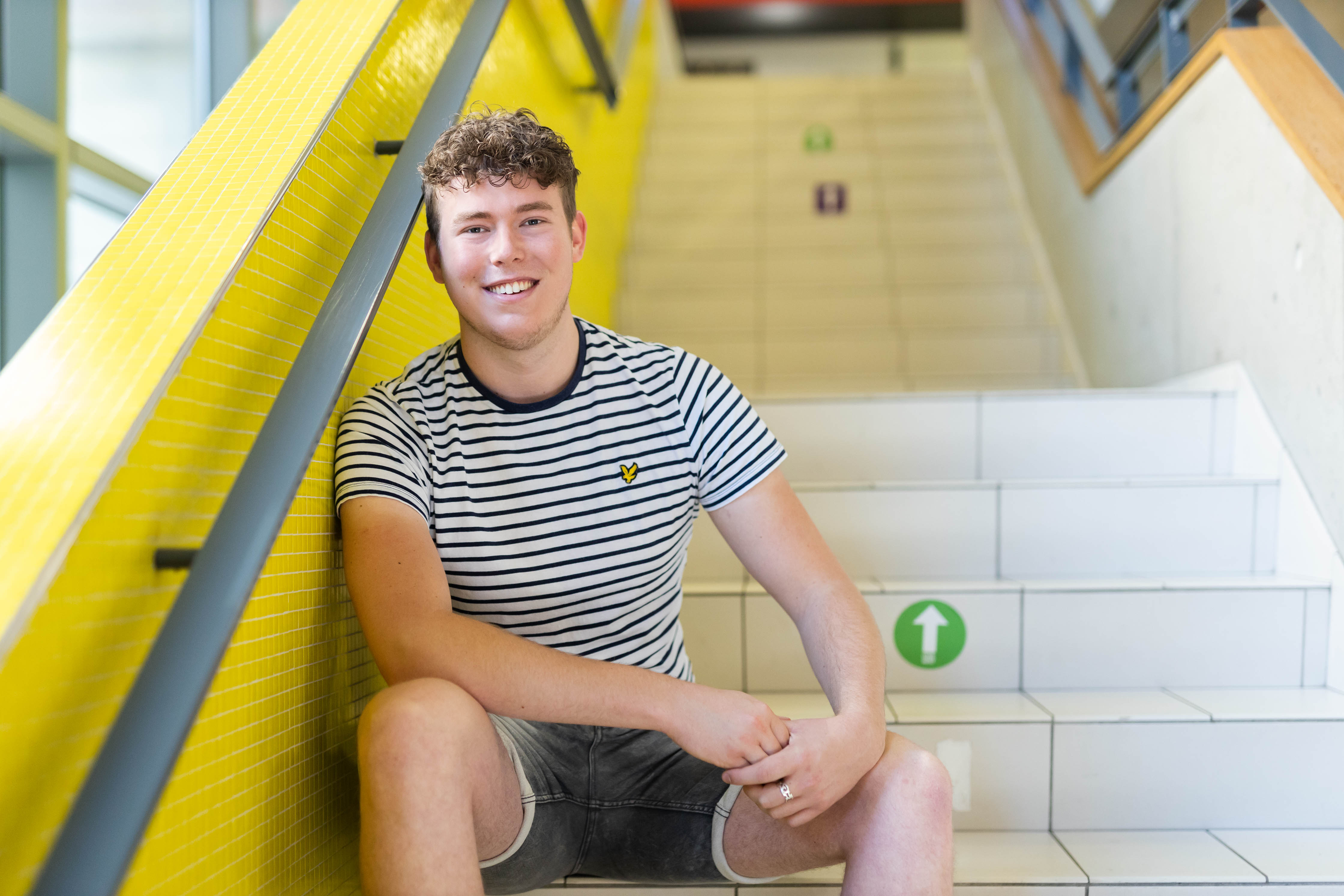 Student ontspant op trap in schoolgebouw, passend bij zorgopleidingsthema van Noorderpoort