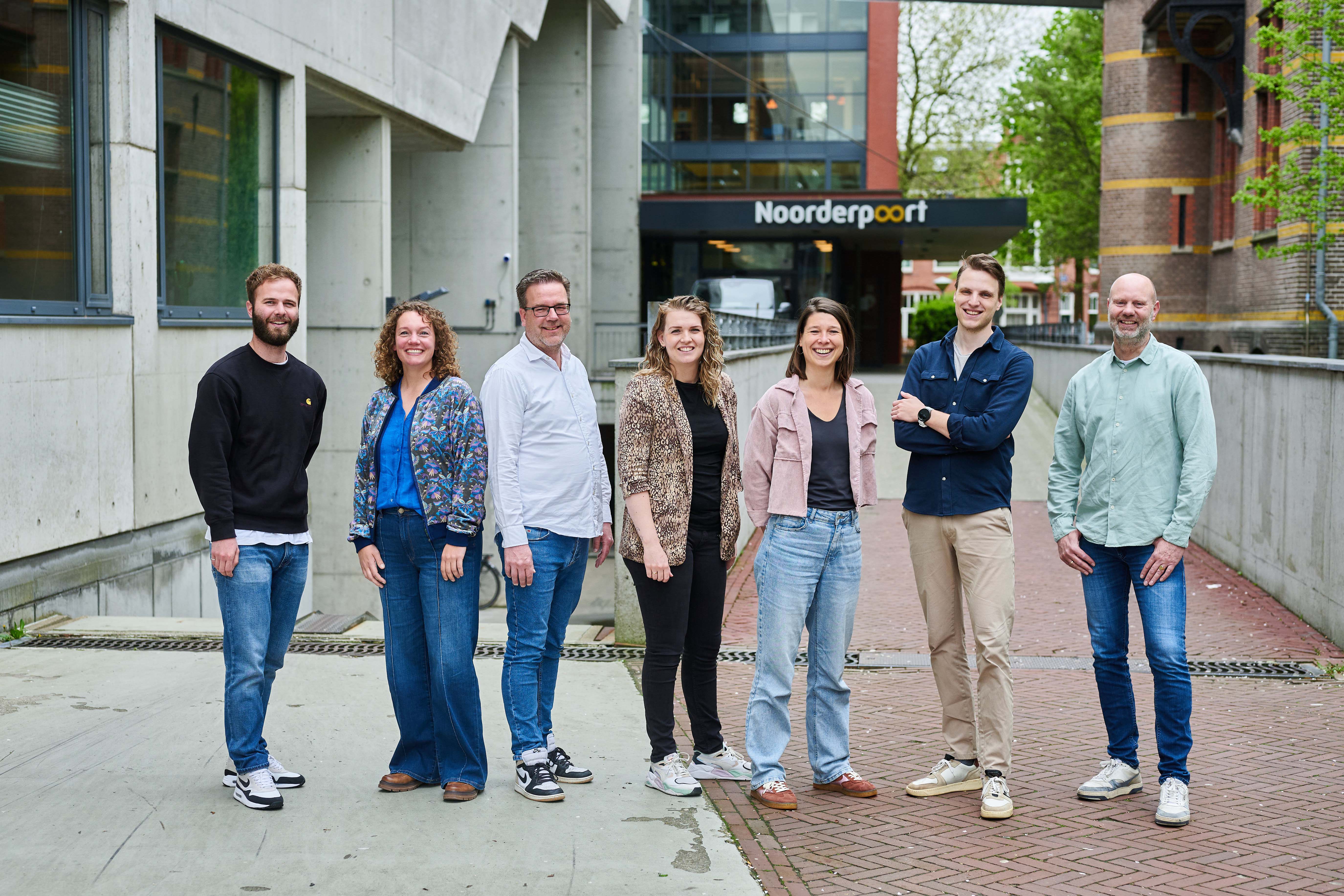 Groep medewerkers van Noorderpoort poseren samen voor de hoofdingang van de onderwijsorganisatie.