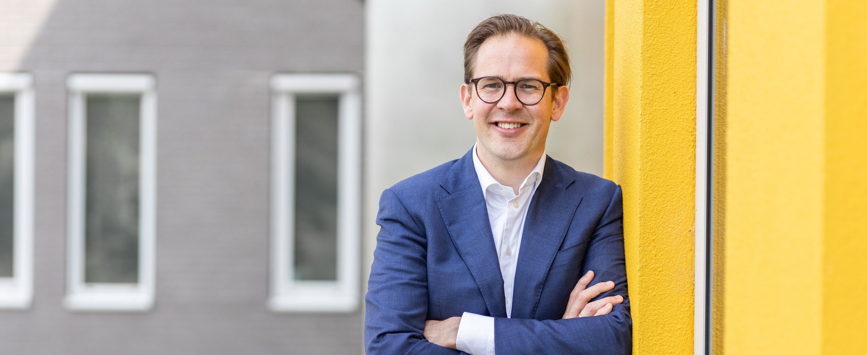 Bestuurder Paul de Rook staat ontspannen met gekruiste armen tegen een geel gebouw bij Noorderpoort