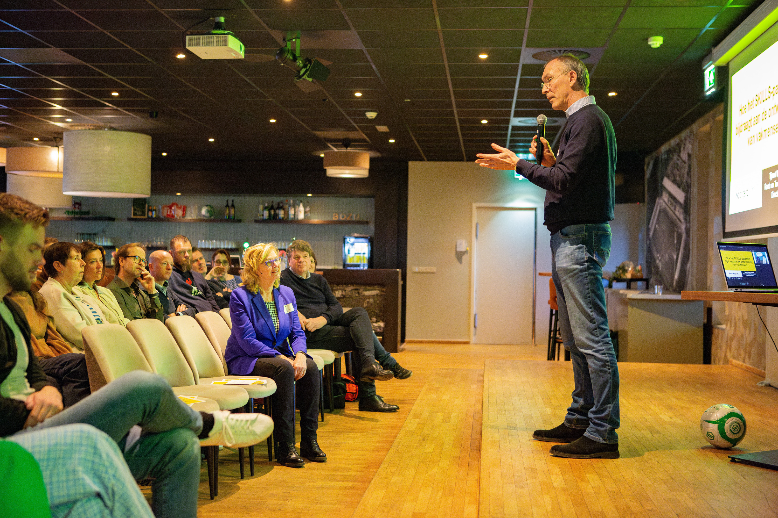 Docent presenteert een interactieve sessie over skillsgericht leren aan een groep studenten en geïnteresseerden.