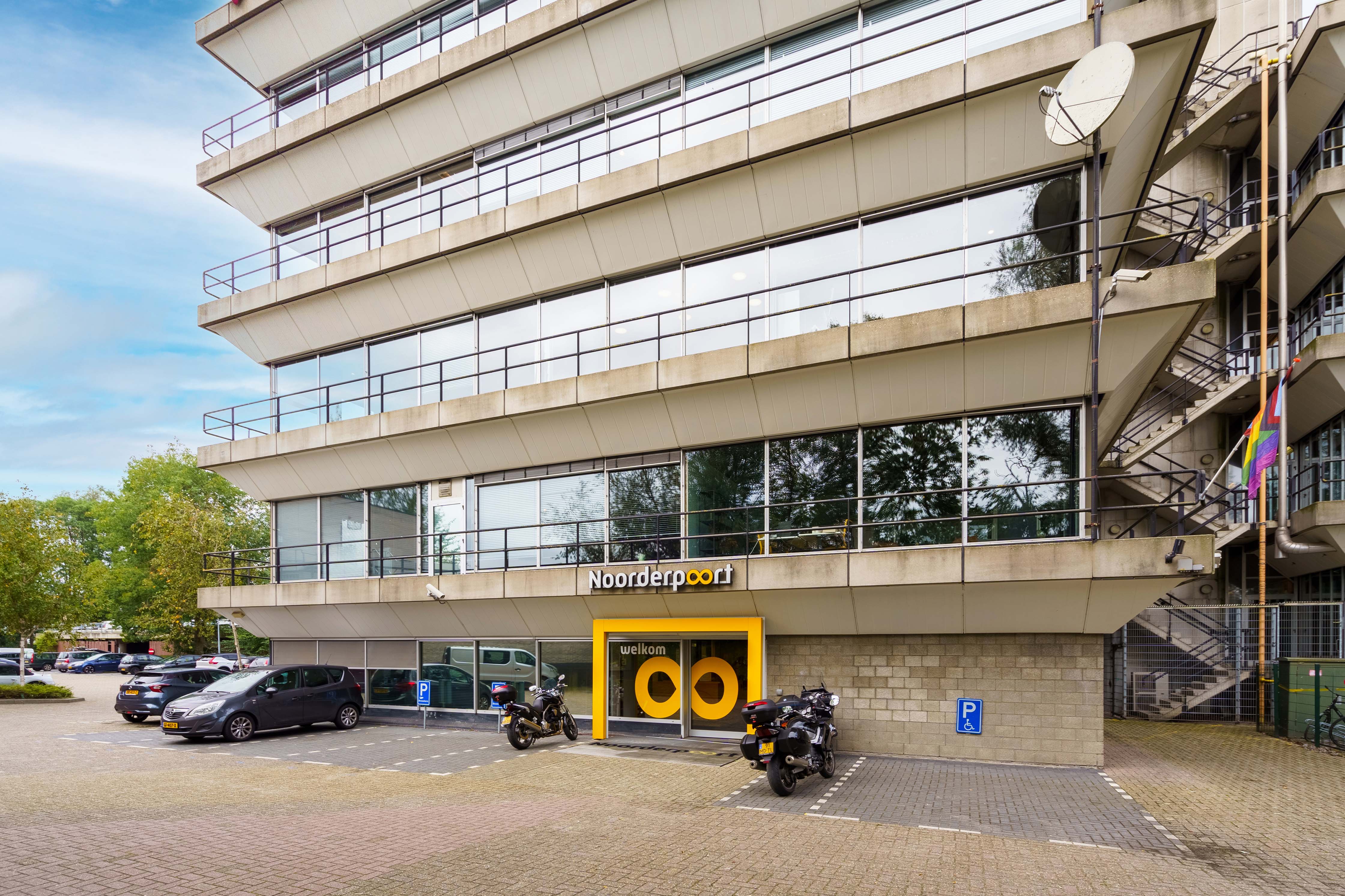 Hoofdingang van Noorderpoort locatie Winschoterdiep 50 in Groningen met parkeerplaatsen en motoren.