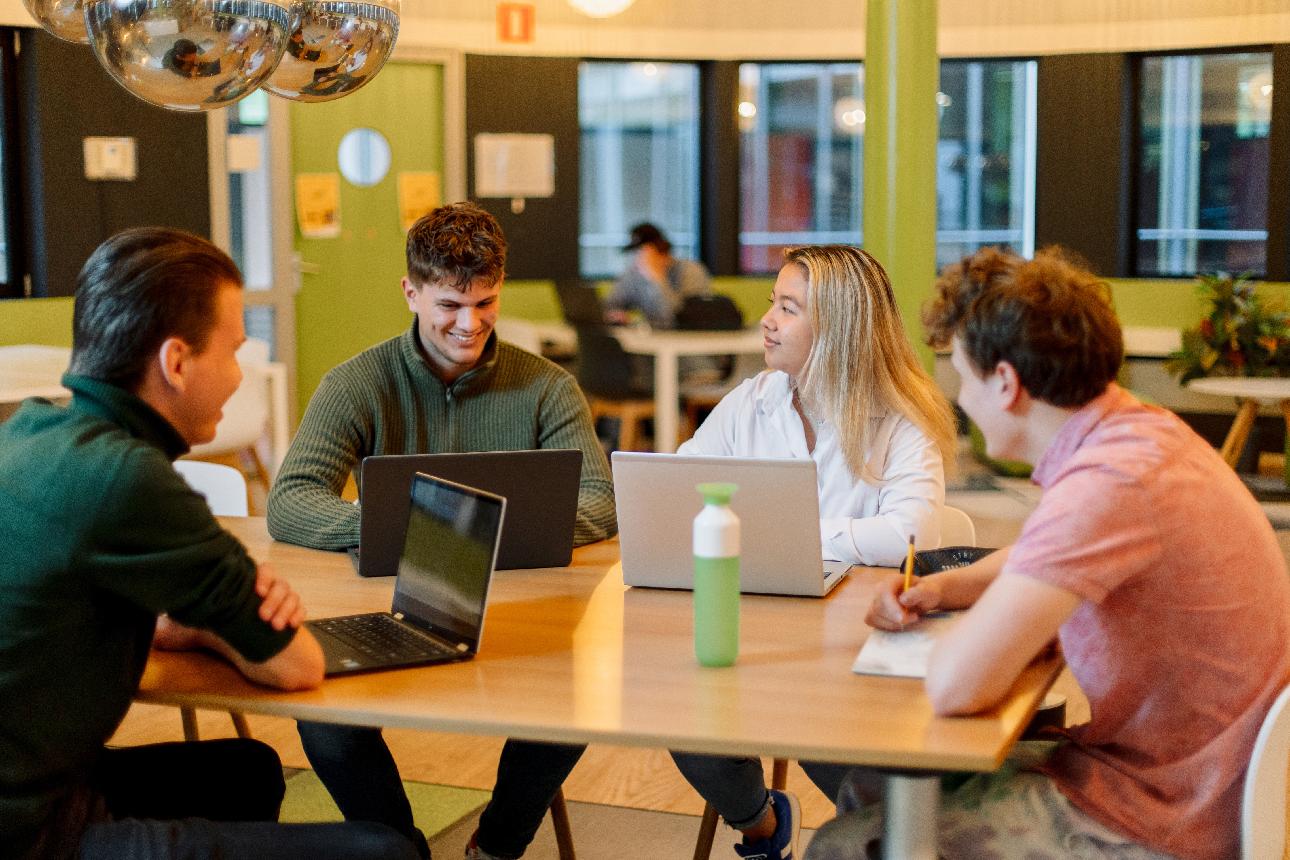 Studenten werken samen aan laptops aan tafel tijdens een specialistenopleiding van Noorderpoort