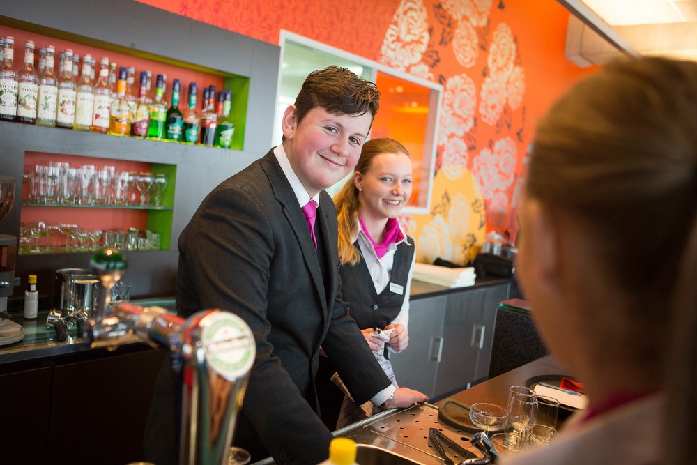 Leerlingen oefenen horecavaardigheden aan een bar in trainingsomgeving passend bij gastvrijheidsonderwijs