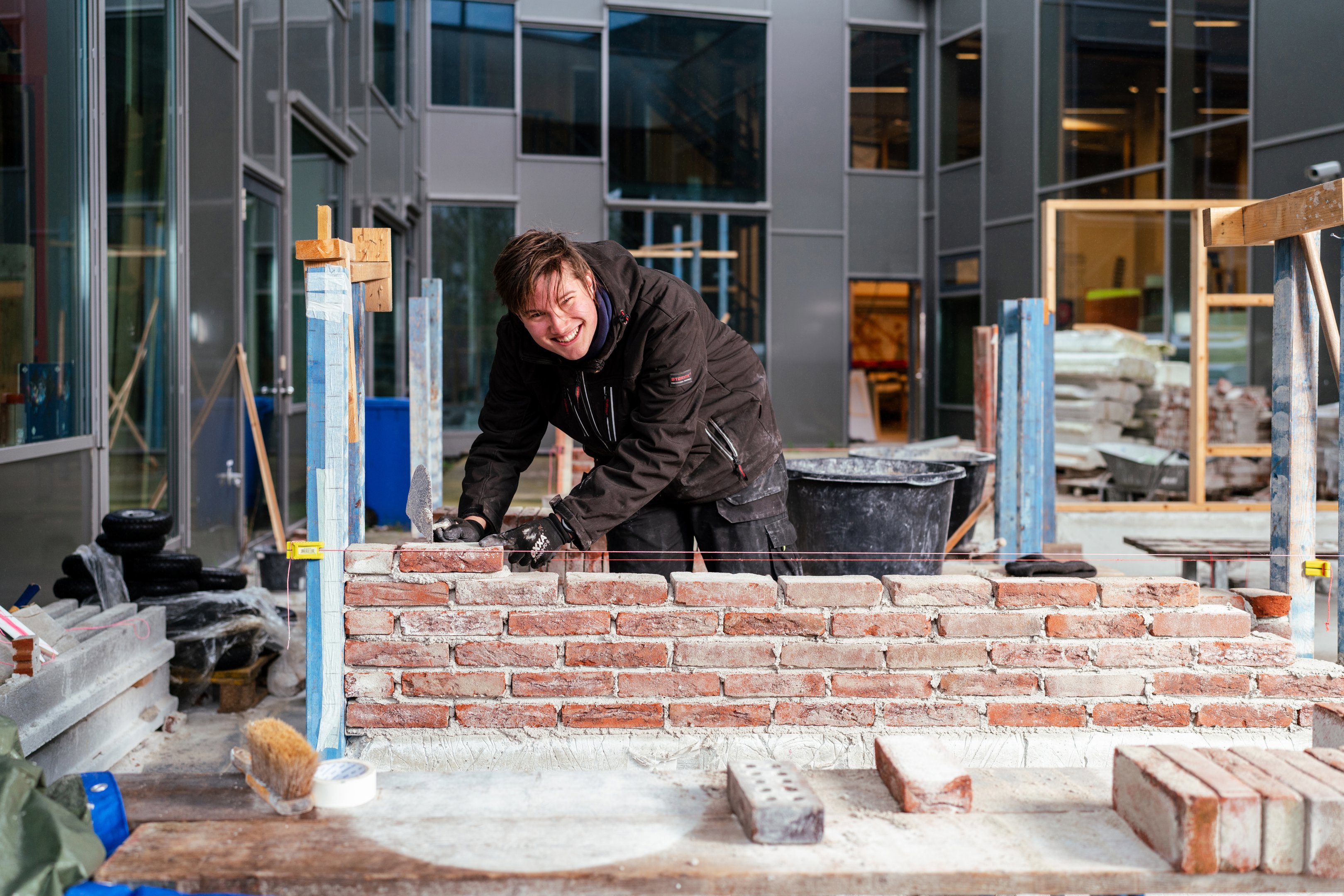 Student-metselaar aan het werk met stenen muur in oefenlokaal voor bouwvakopleidingen.