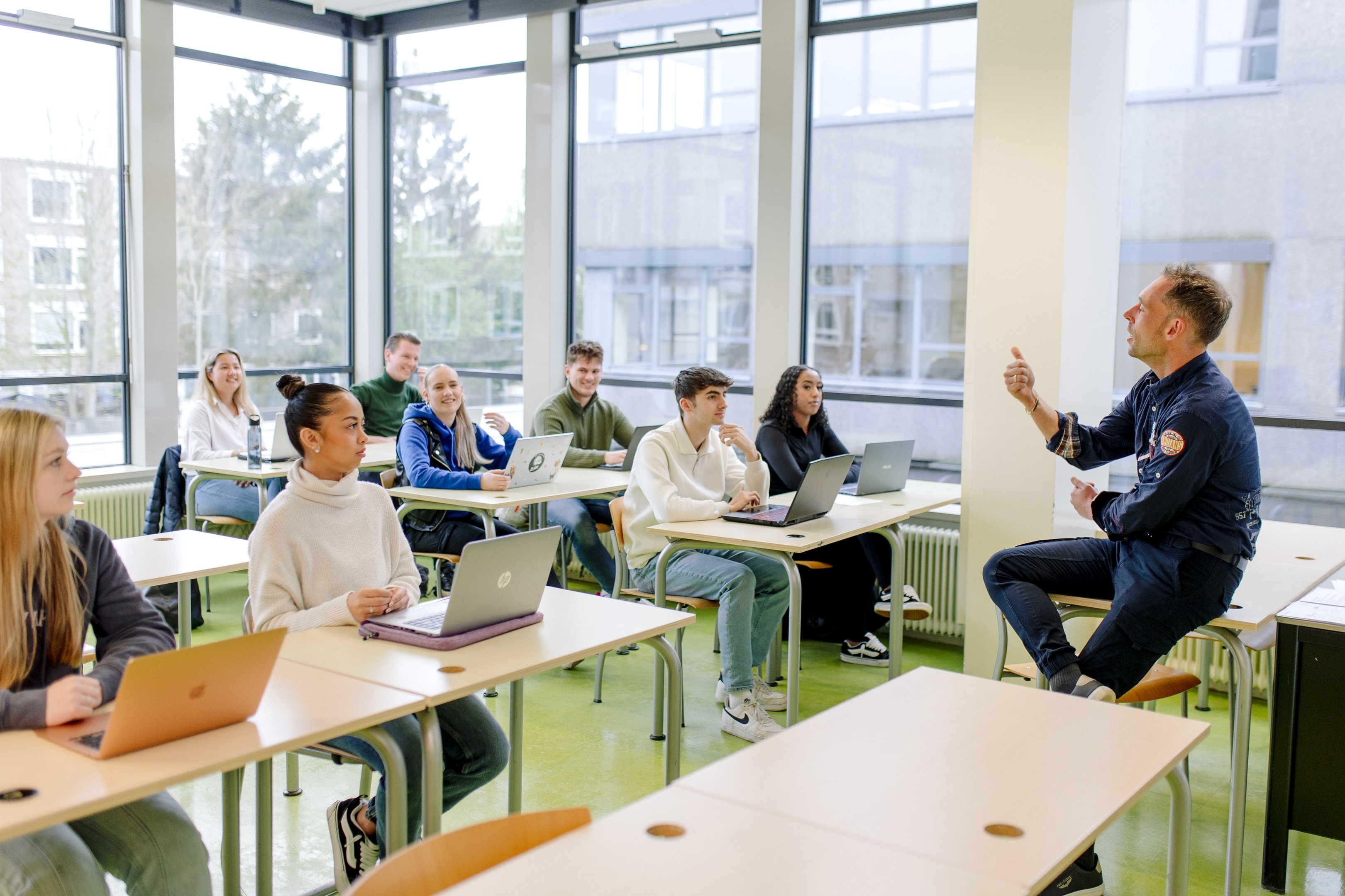 Docent geeft les aan betrokken studenten die met laptops deelnemen in een lichte klasomgeving