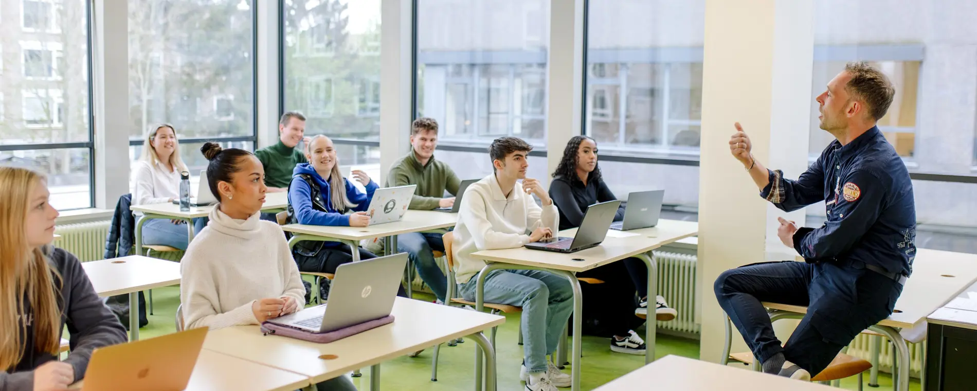Docent geeft les aan betrokken studenten die met laptops deelnemen in een lichte klasomgeving