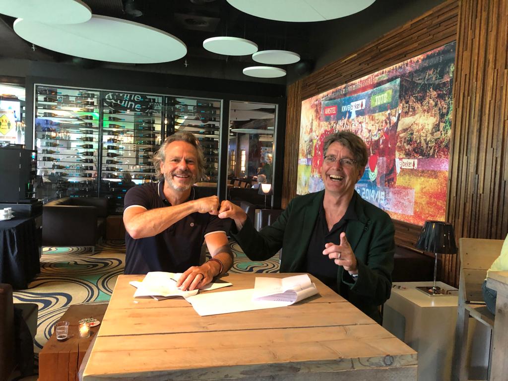 Twee mannen ondertekenen een samenwerkingsovereenkomst voor de opleiding Acteur in een moderne vergaderruimte.