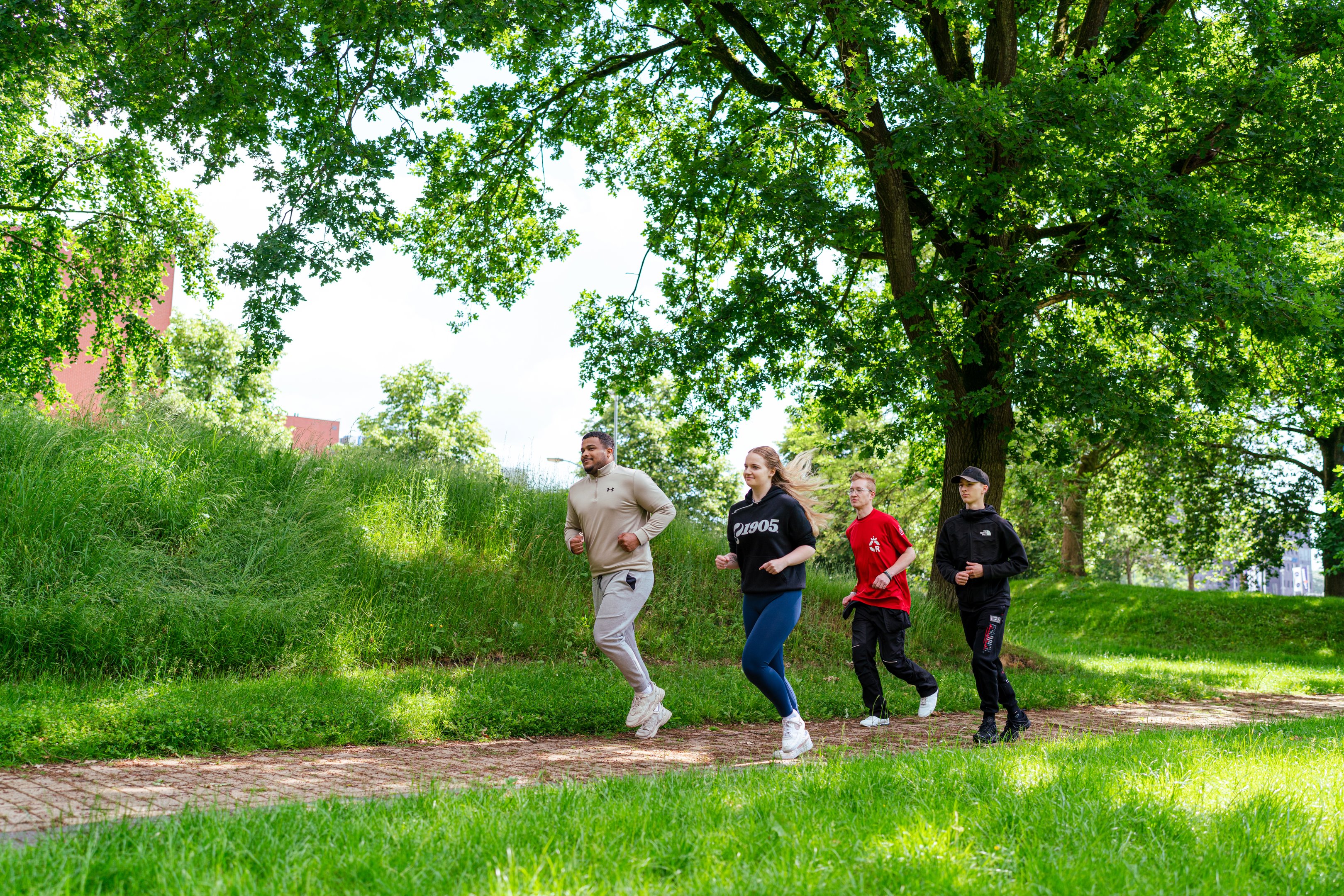 Vier personen joggen samen op een pad in een groene omgeving, gericht op sportieve veiligheid en welzijn.