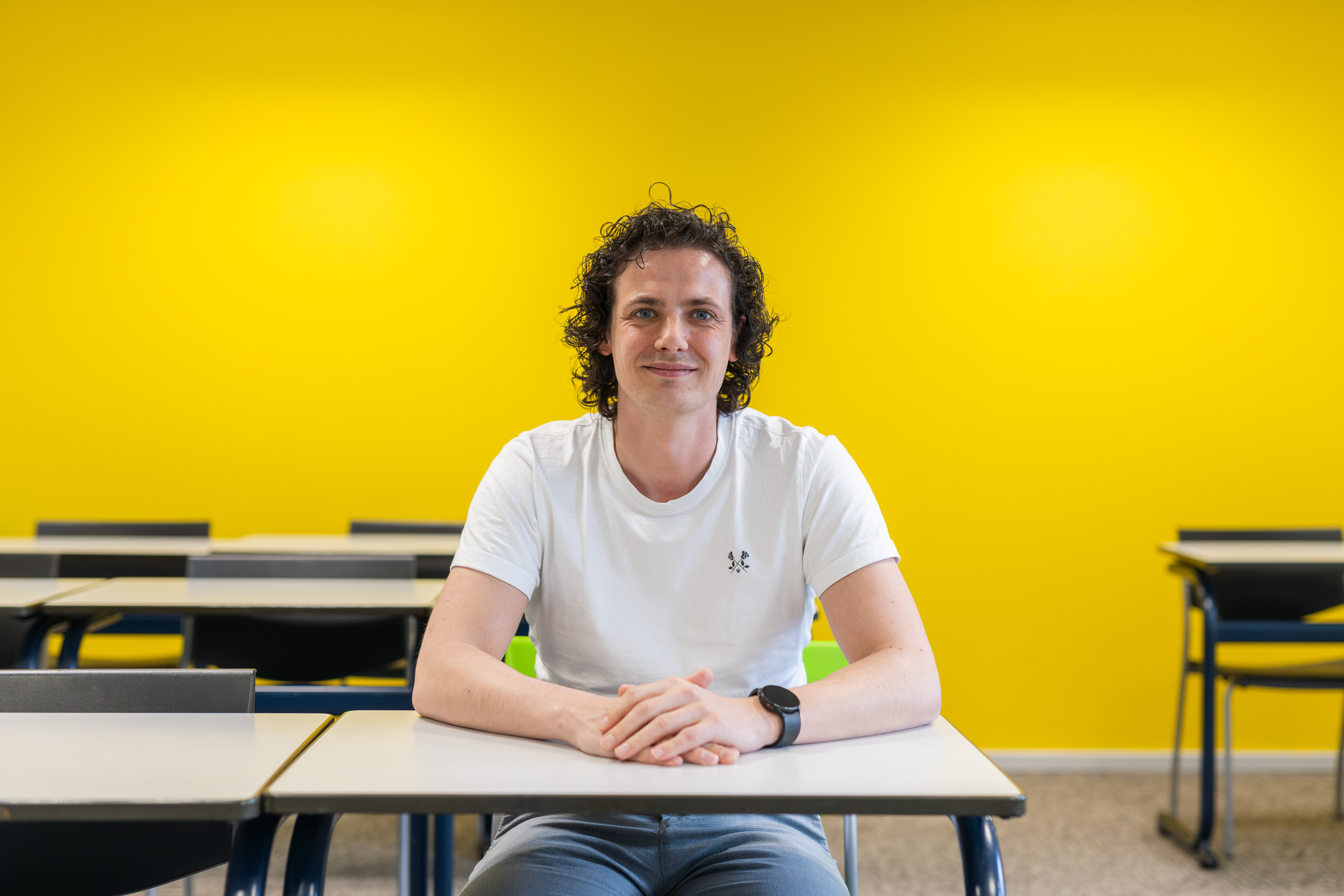 Student zit aan tafel in klaslokaal met gele achtergrond, klaar om te leren en groeien binnen Noorderpoort.