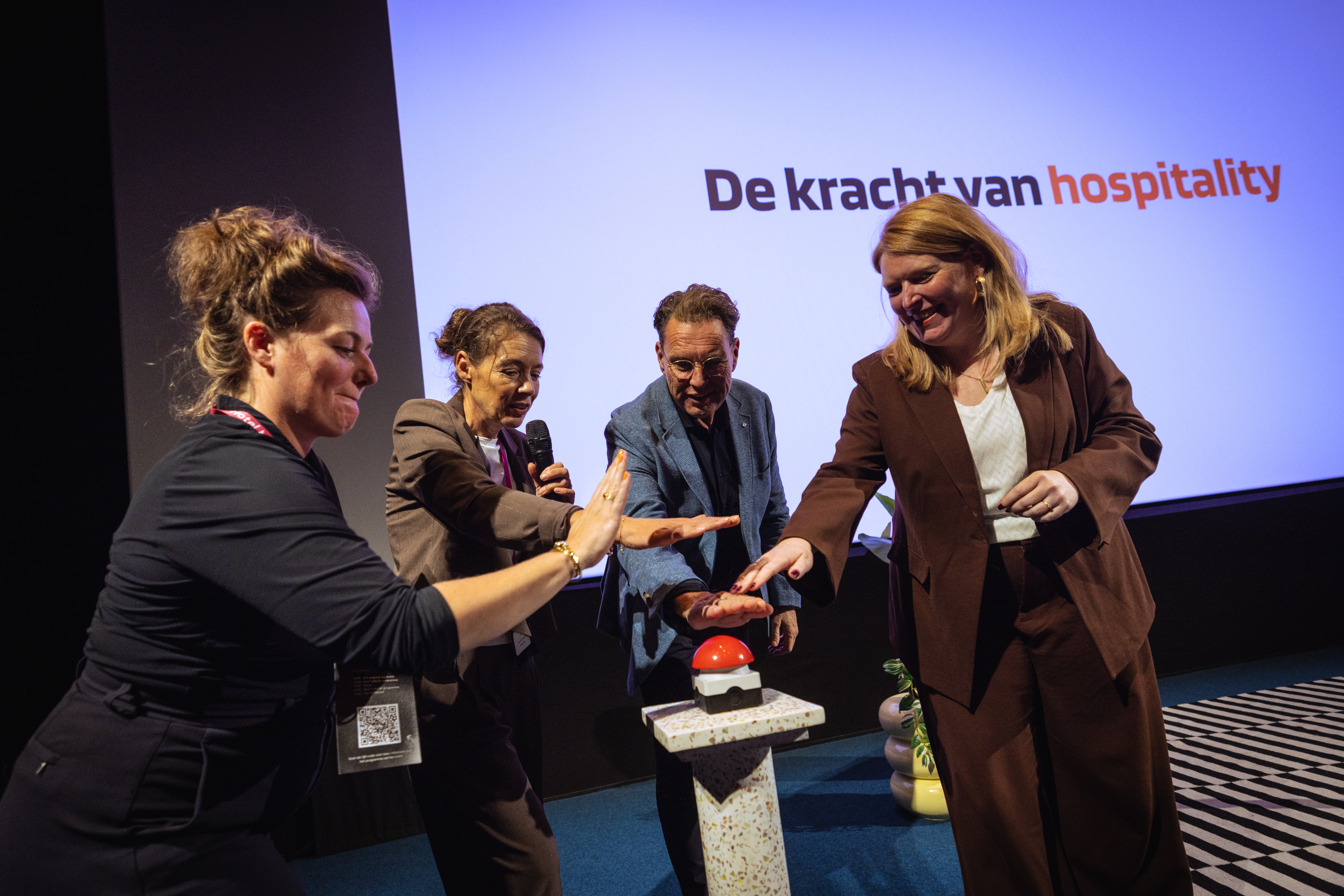 Vier professionals activeren gezamenlijk een rode knop tijdens een evenement over de toekomst van hospitality in Noord-Nederland.