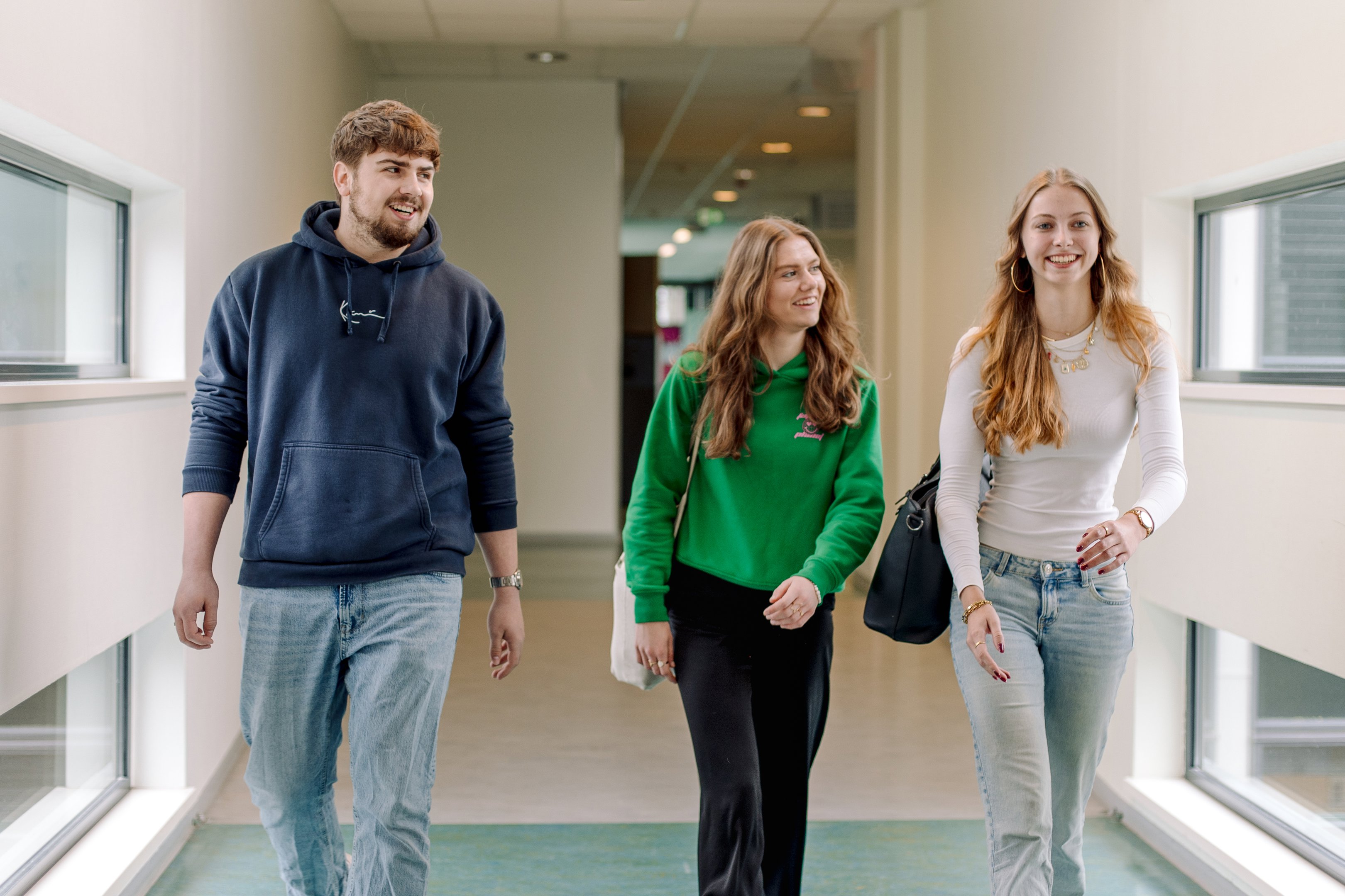 Drie studenten lopen samen in een gang binnen een onderwijsgebouw van Noorderpoort.