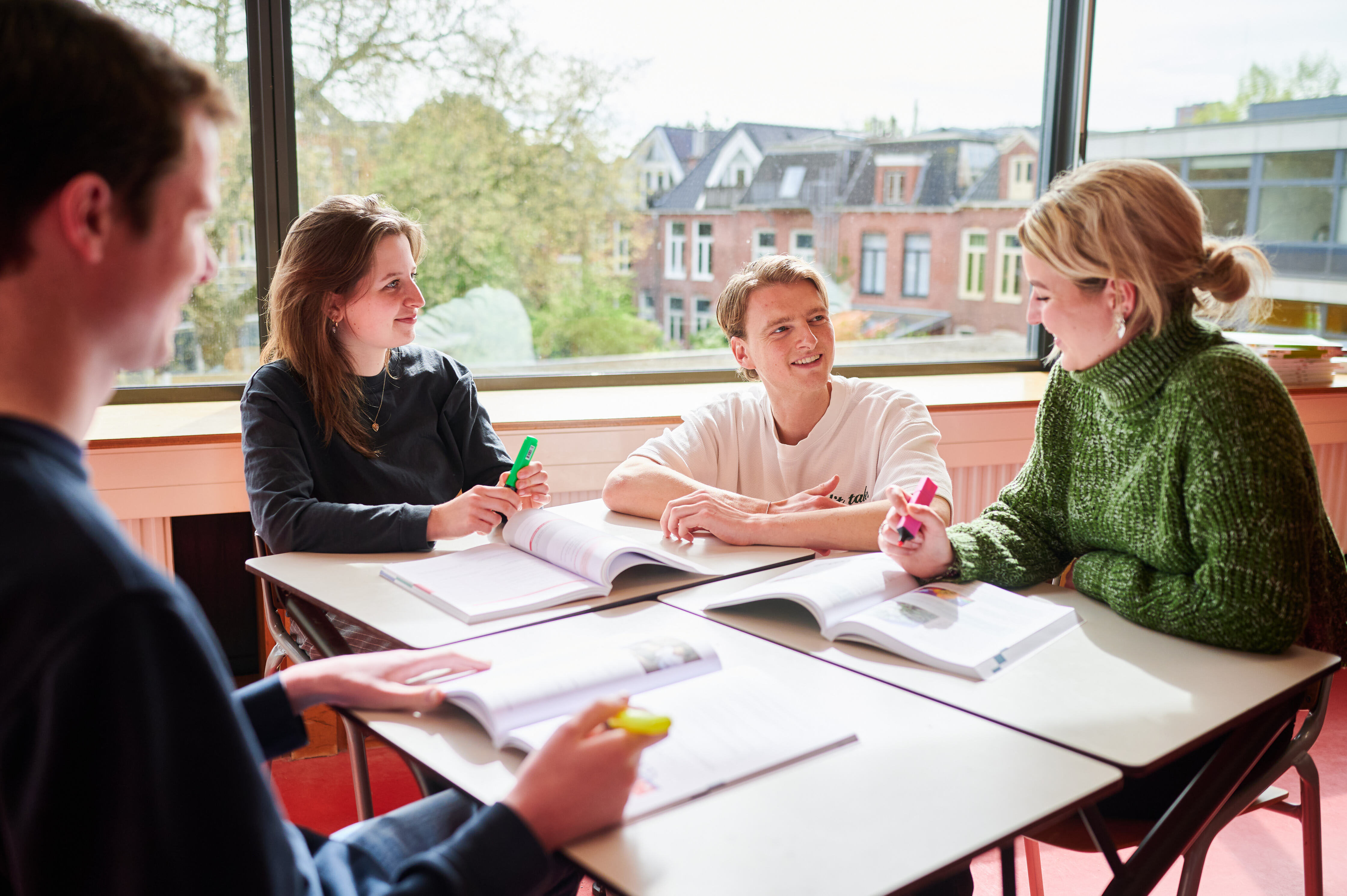 Studenten in een studiegesprek met een docent rondom een tafel met open boeken en markeerstiften