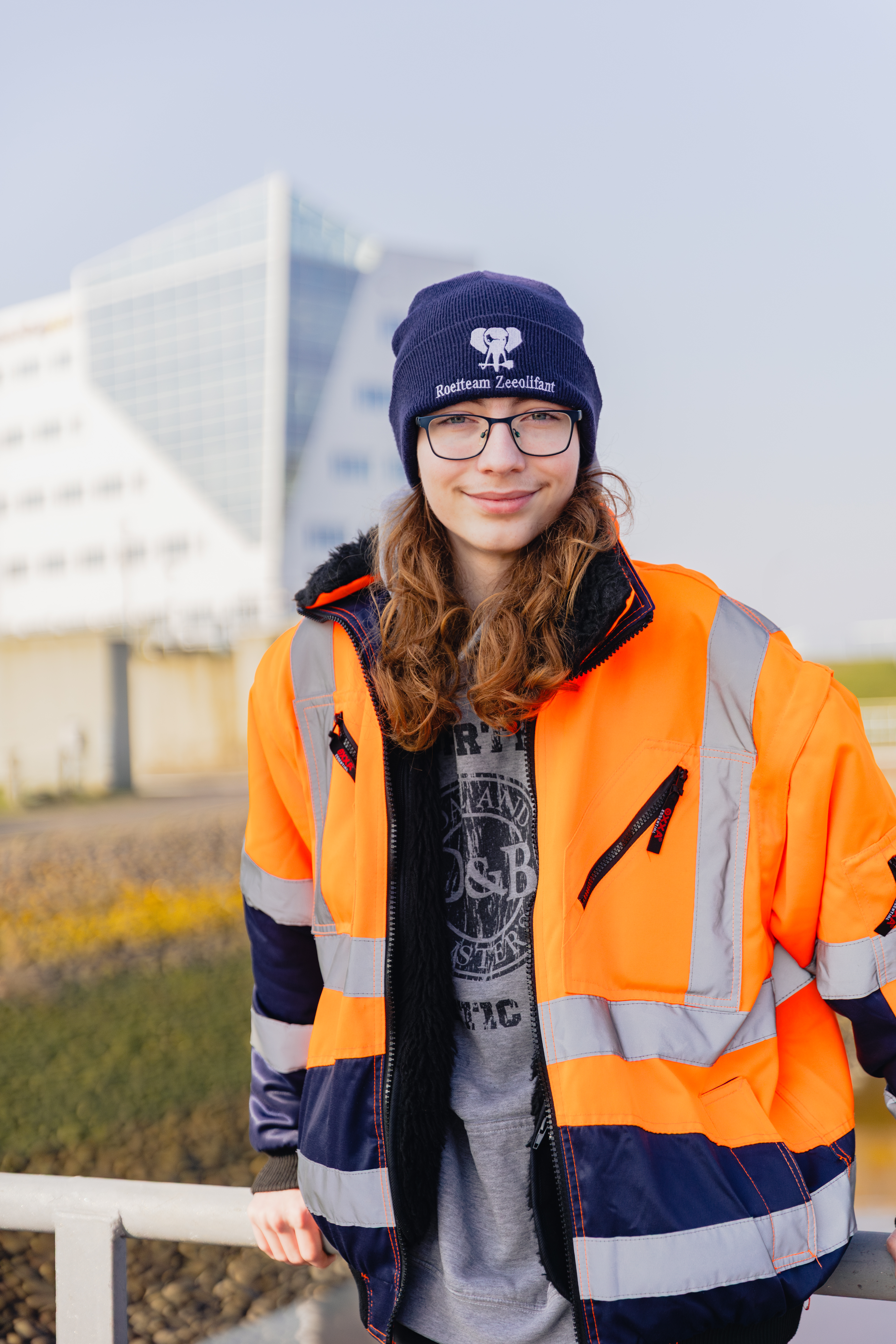 Student in veiligheidsjas en muts buiten bij een modern gebouw, symbool voor diverse mbo-routes.