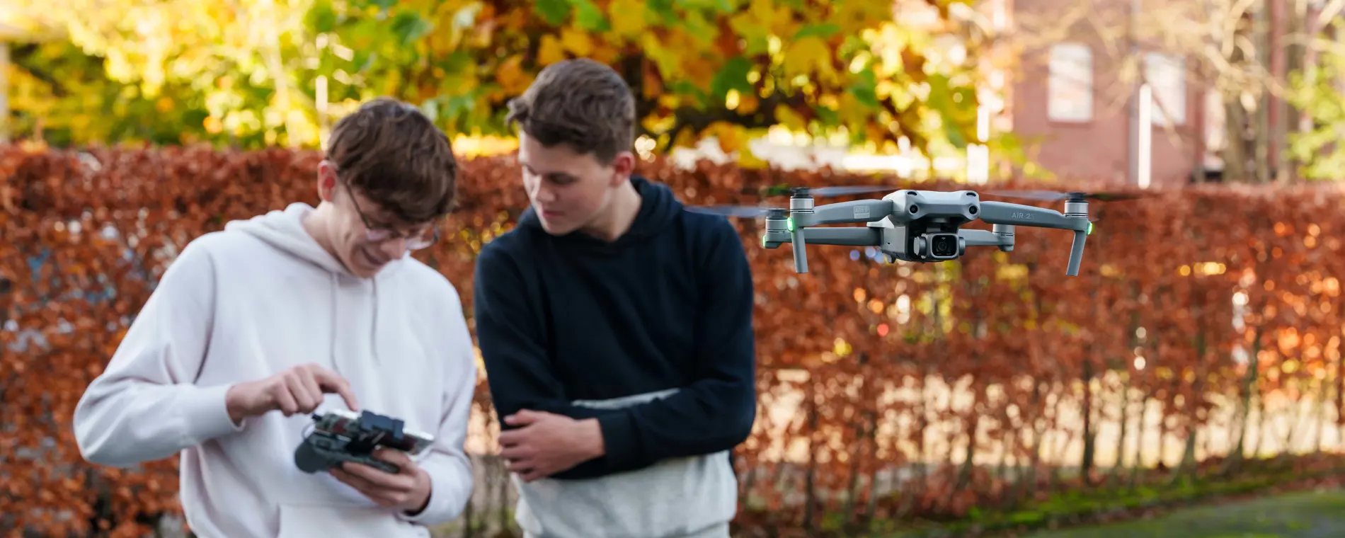 Twee studenten bedienen een drone met een afstandsbediening tijdens een praktijkles buiten