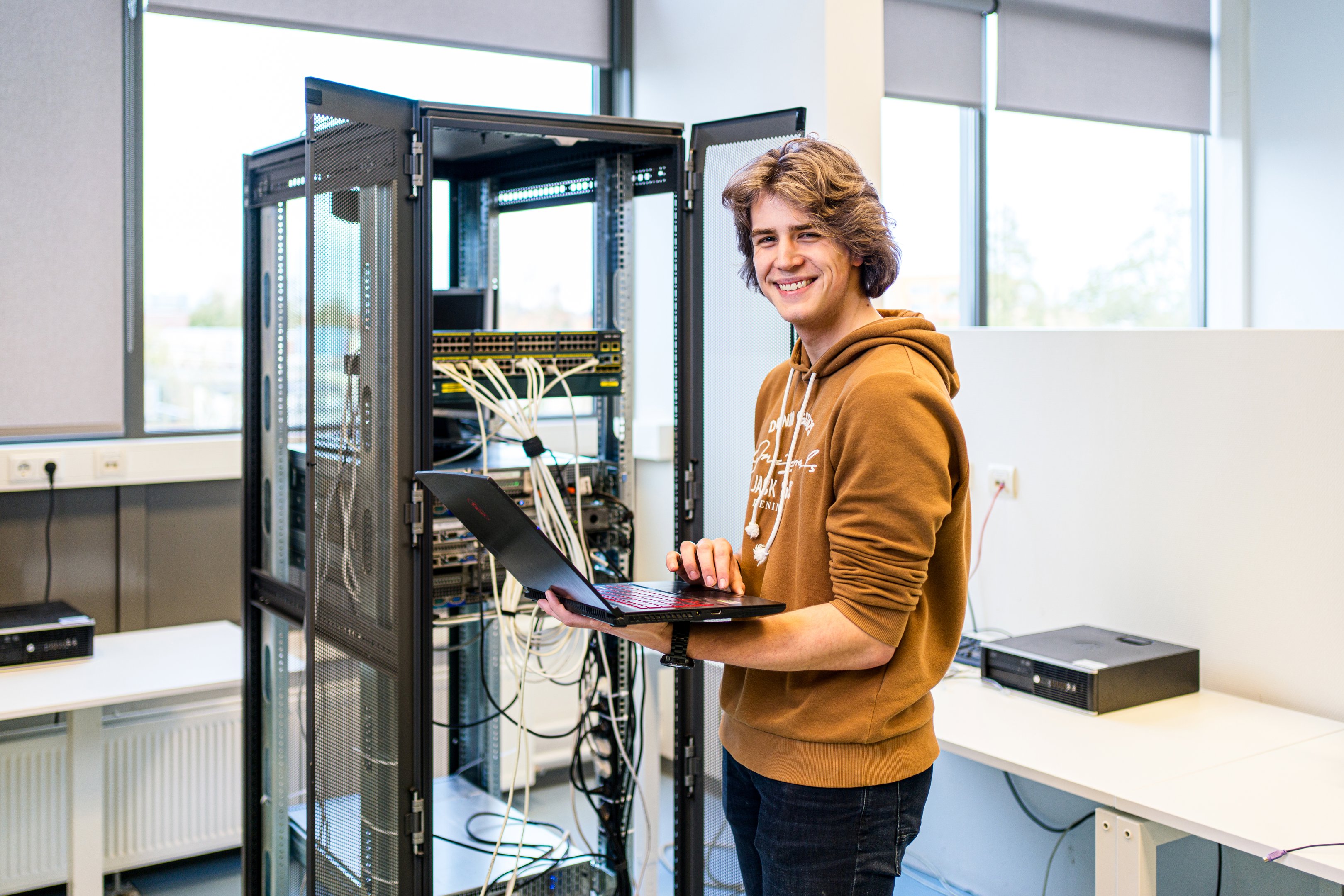 Student bekijkt gegevens op laptop bij serversysteem in computerruimte
