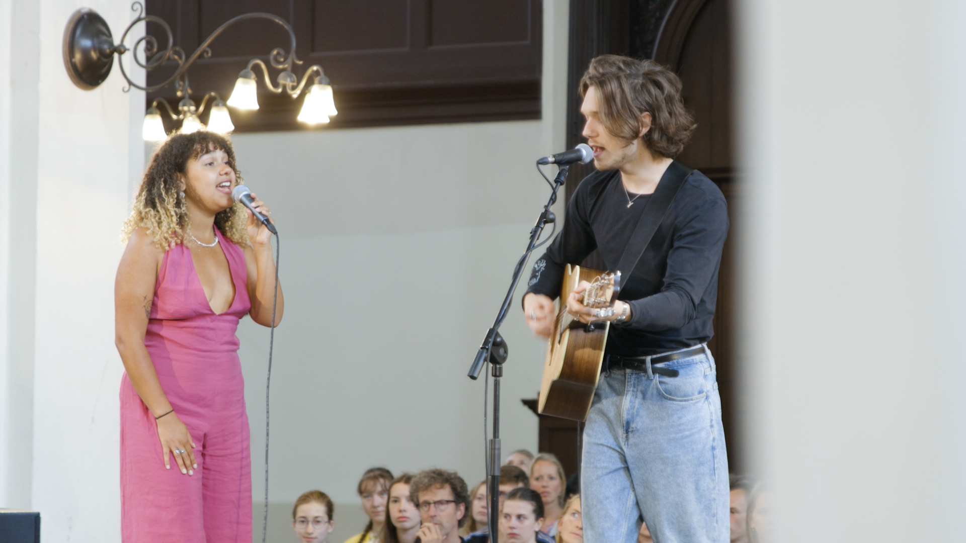 Twee muzikanten verzorgen liveoptreden tijdens Keti Koti-event, met studenten en medewerkers in kerkelijke omgeving