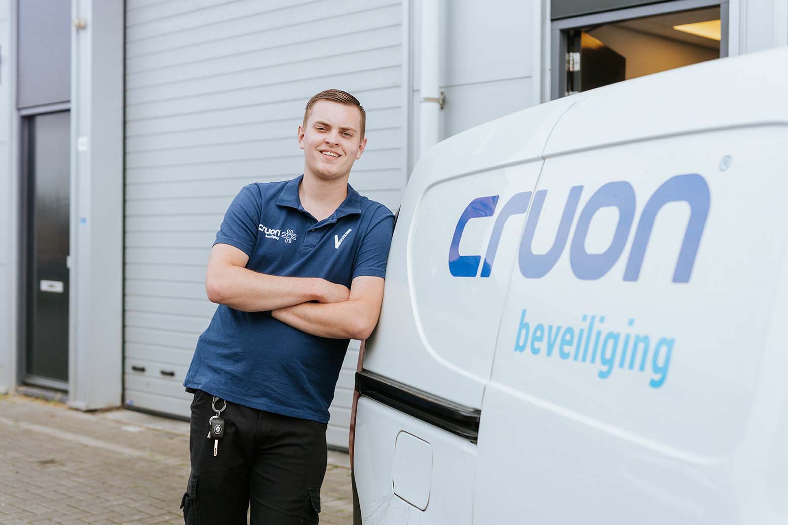 Beveiliger staat met armen over elkaar naast een voertuig met logo van een beveiligingsbedrijf.