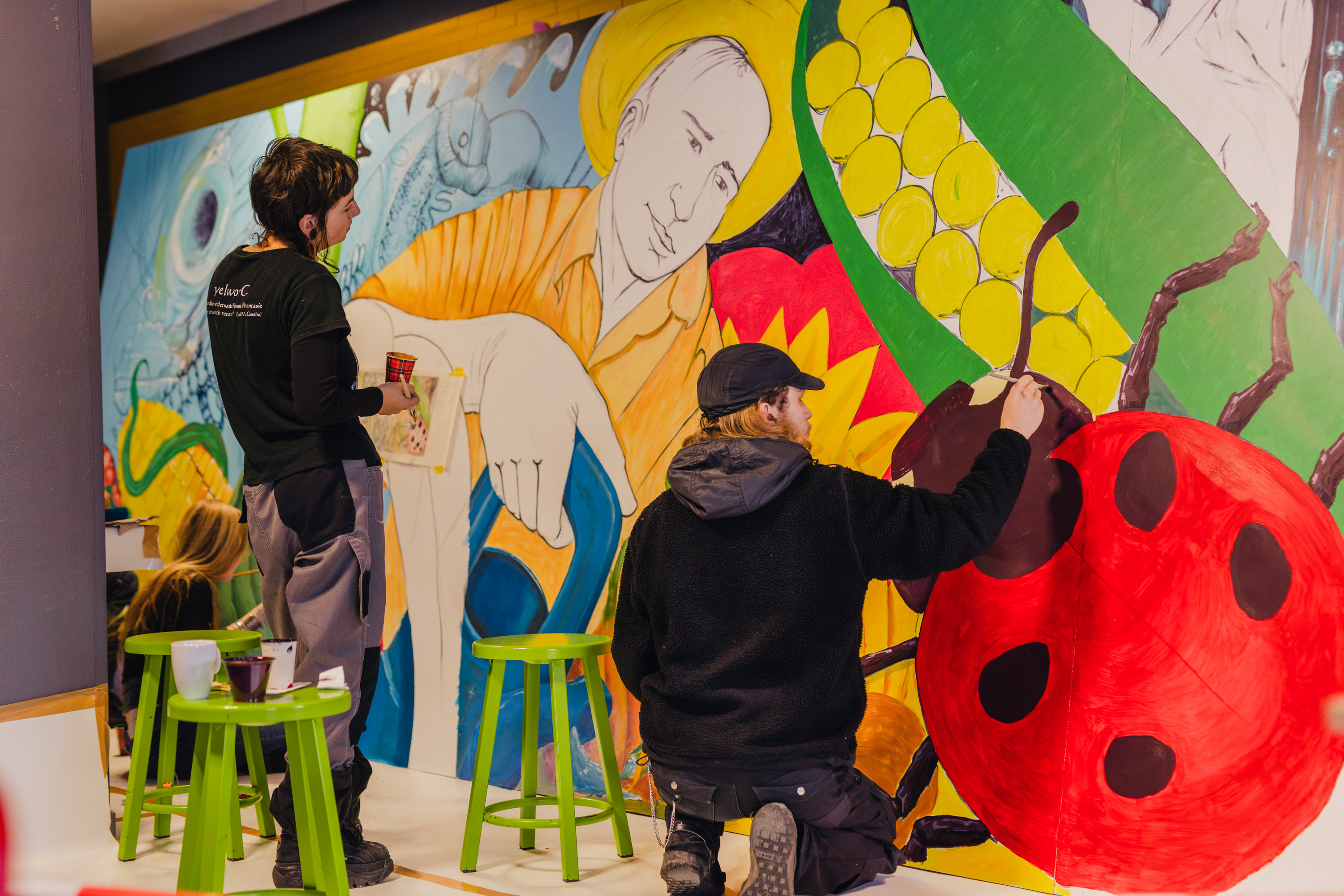 Mbo-studenten werken samen aan kleurrijke muurschildering met natuur- en wetenschappelijke thema’s.