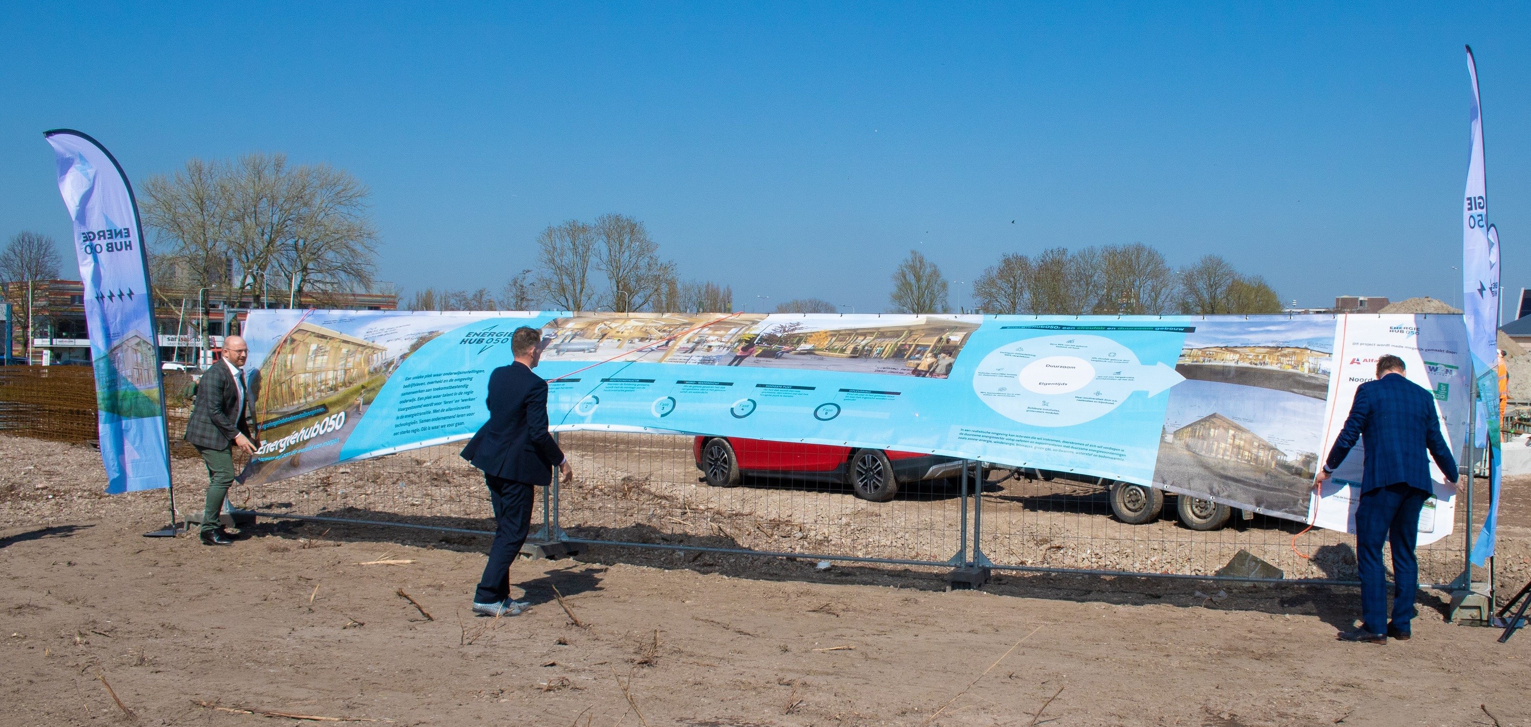 Drie vertegenwoordigers bij onthulling van bouwdoek met plannen voor Energiehub050 op bouwlocatie