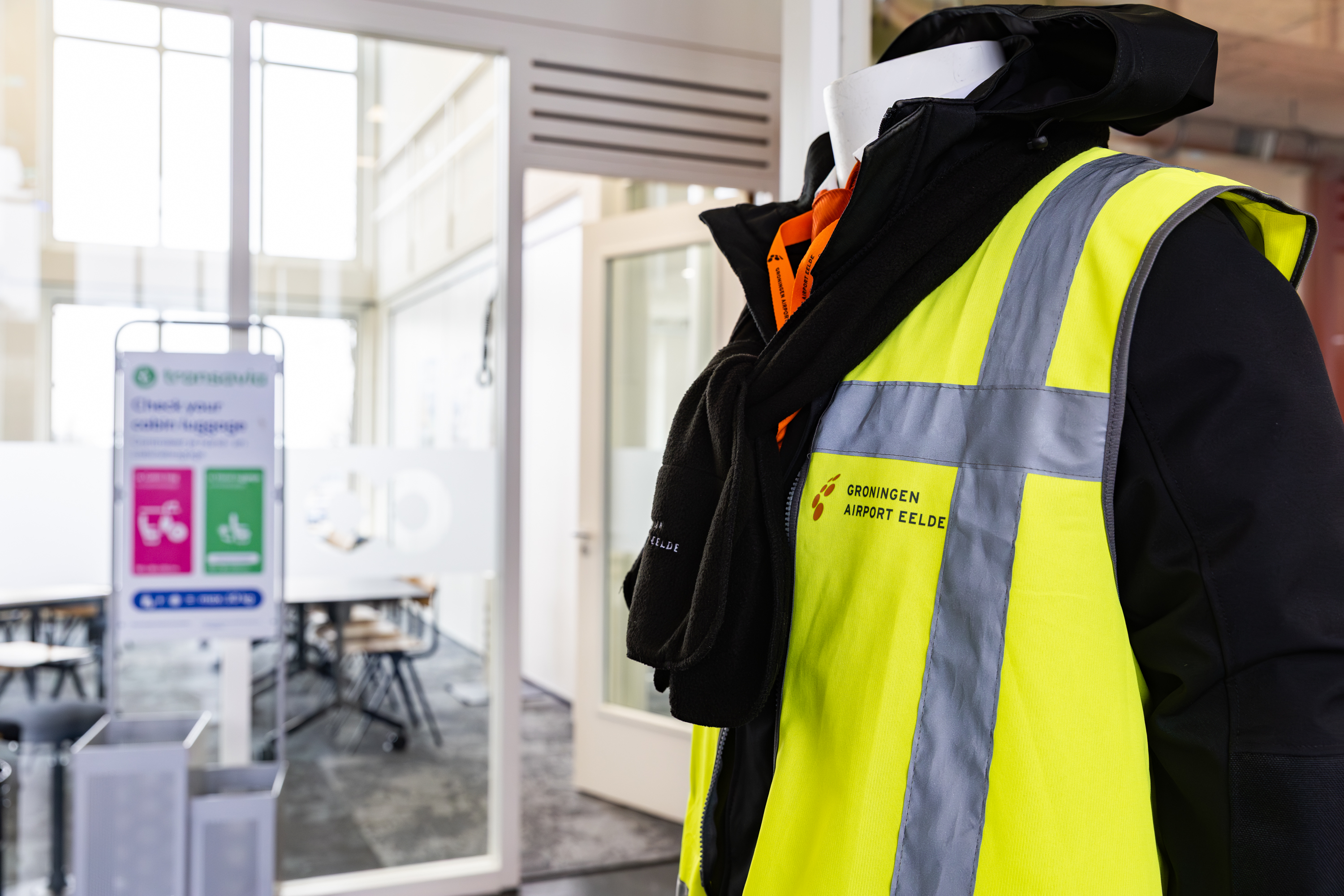 Persoon draagt een reflecterend veiligheidsvest met logo Groningen Airport Eelde in een lesruimte van Noorderpoort